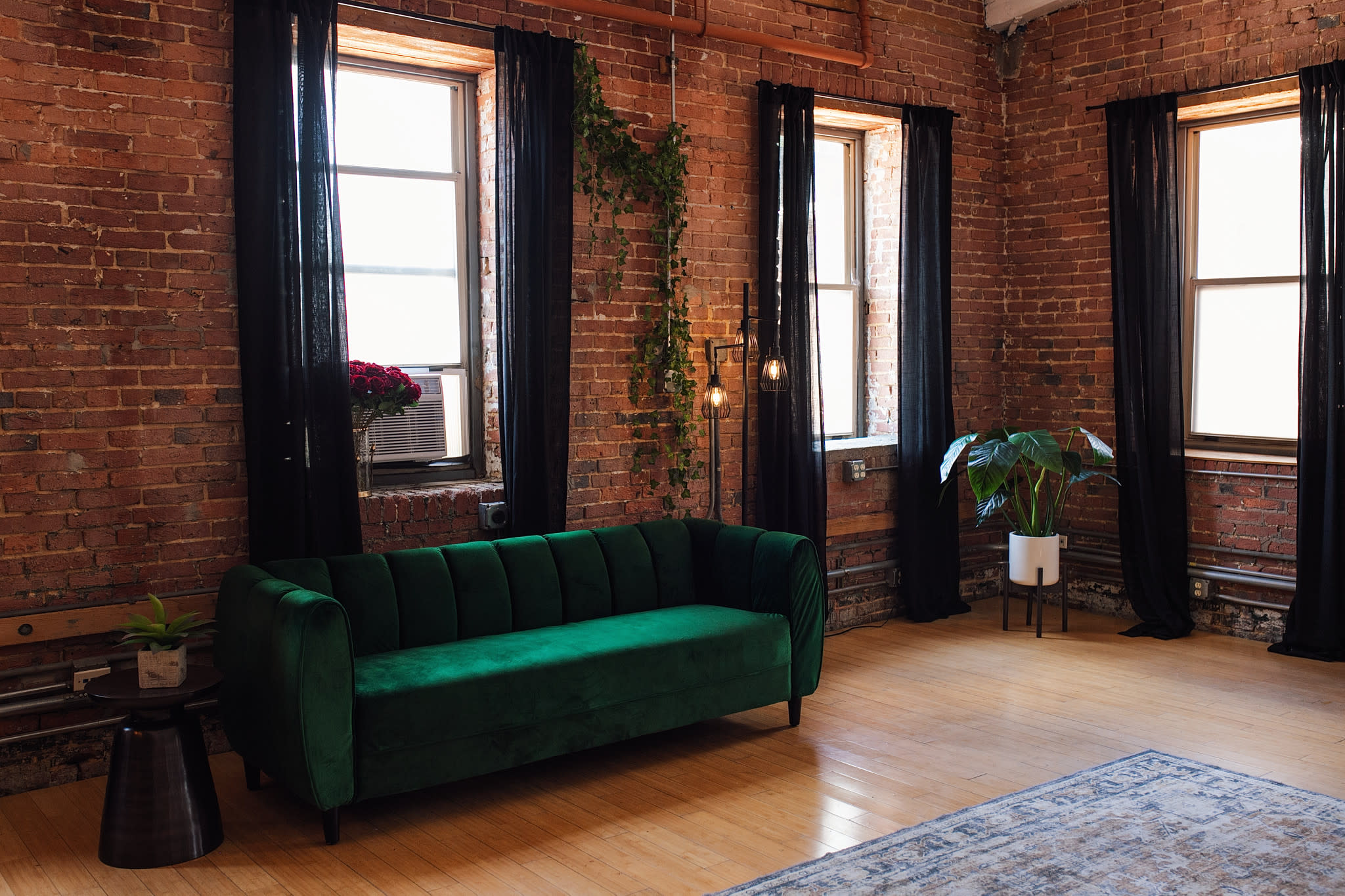 A photographer captures a model in front of a green couch during a photoshoot in a brick-walled studio.