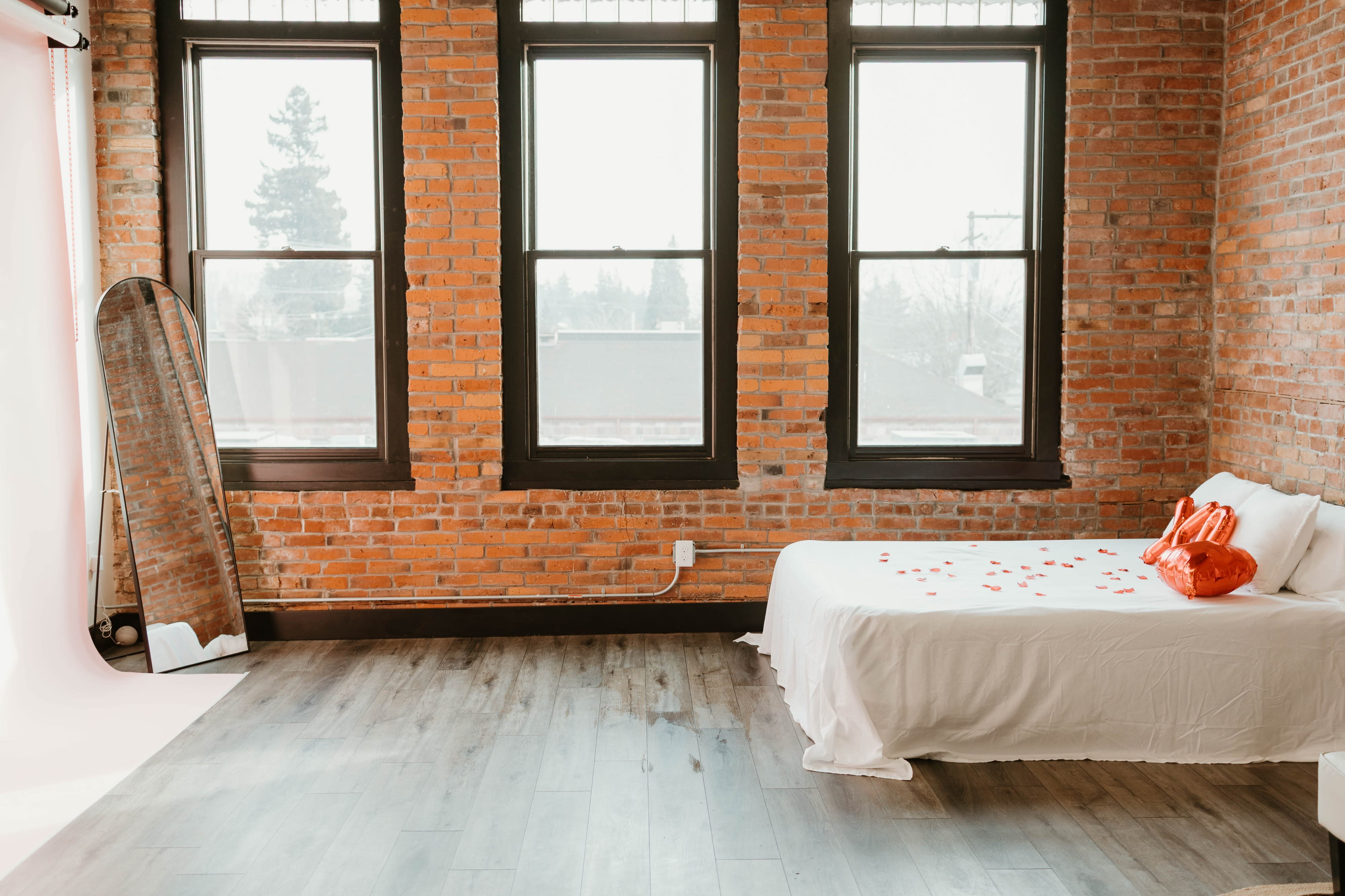A person is posing in front of a large mirror in a room featuring exposed brick walls and a minimalist setup.