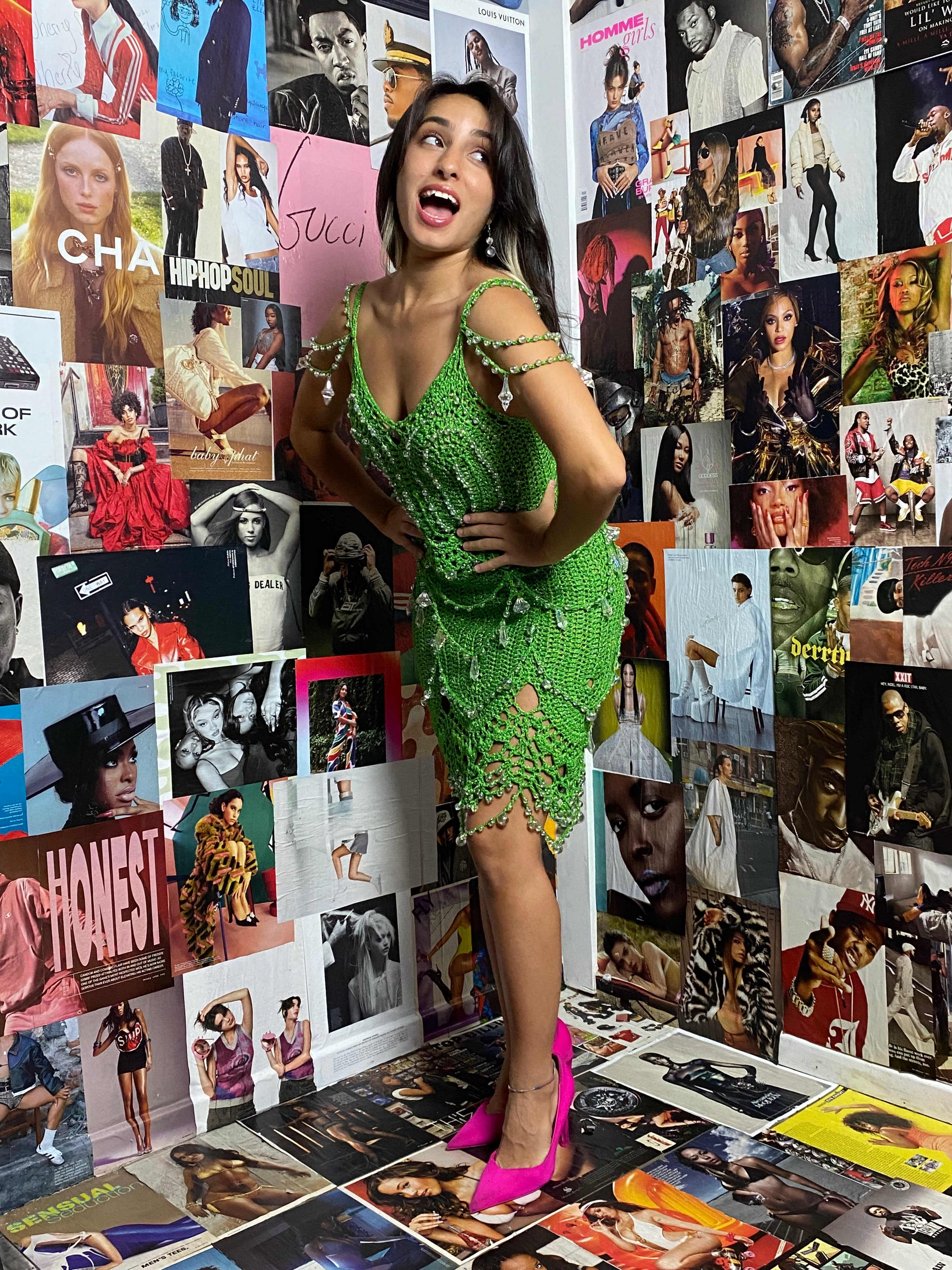 A model poses on the floor in a pink dress, holding a cake adorned with cherries, amidst shiny decorations and disco balls.
