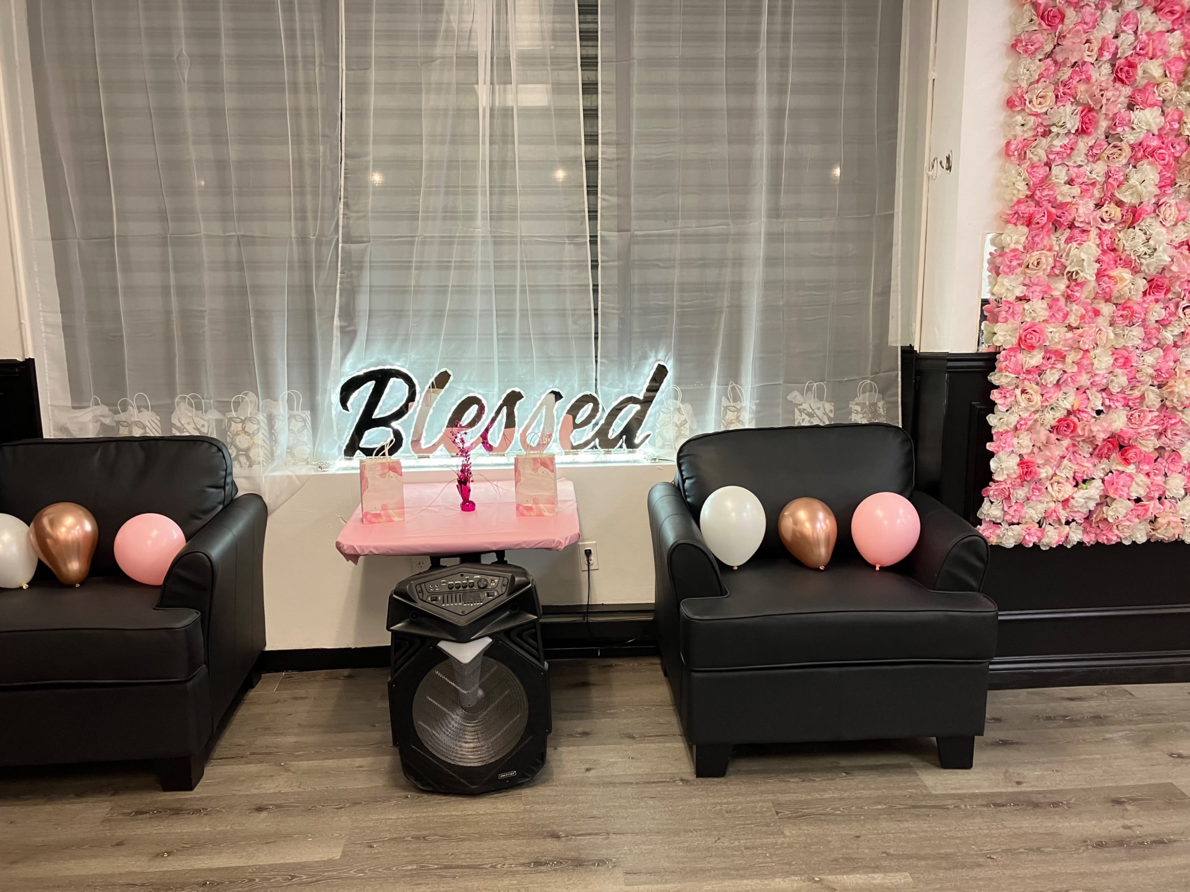 The image shows a decorated room set up for a bridal shower, featuring a long table with pink and gold accents, clear chairs, and a large white throne-like chair in the corner.