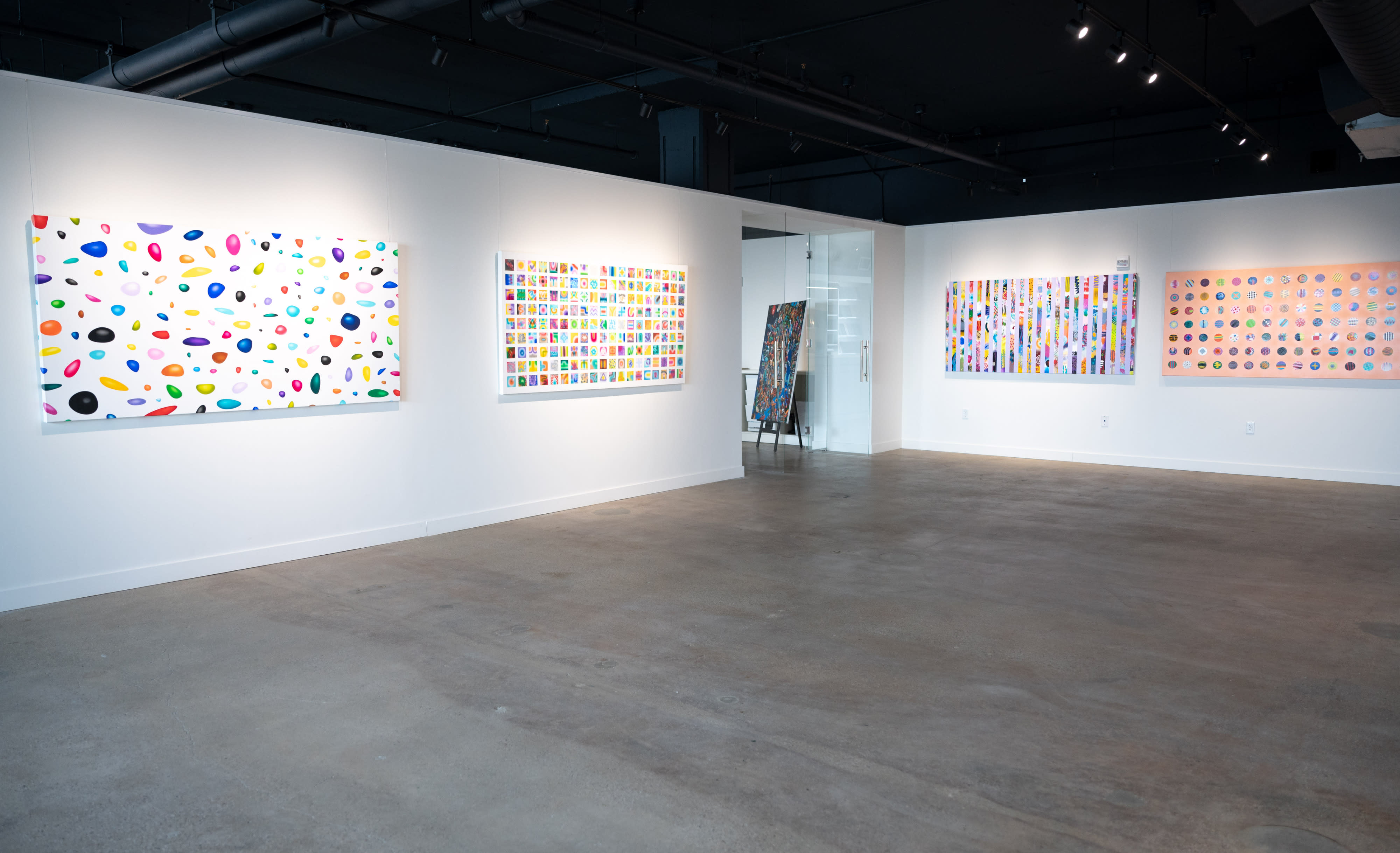 An album release party is taking place in a modern art gallery, featuring various artworks displayed on the walls and a sound setup in the corner.