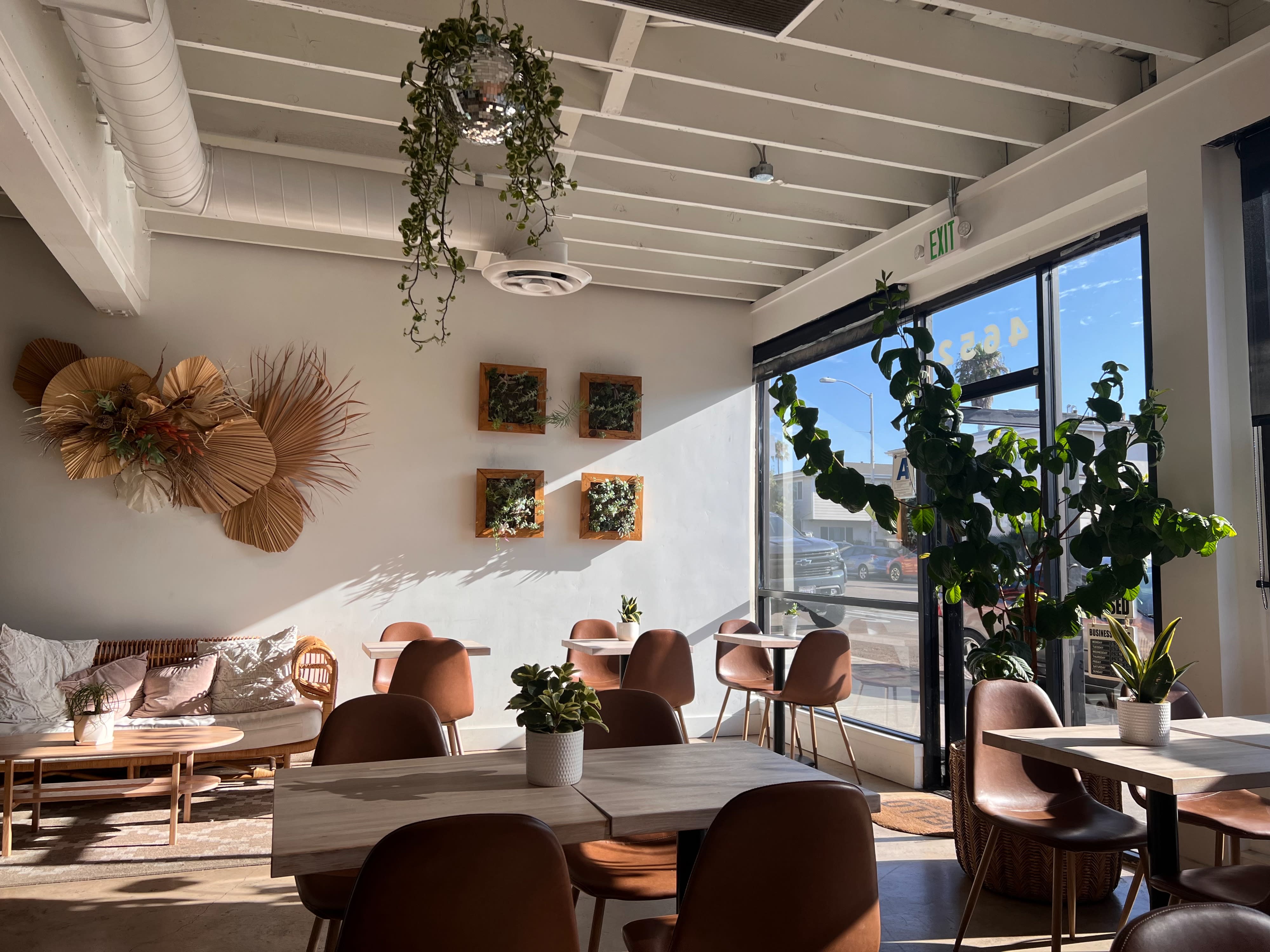 A cozy venue is decorated with a “Bride to Be” banner, floral arrangements, and minimalist seating for a bridal event.