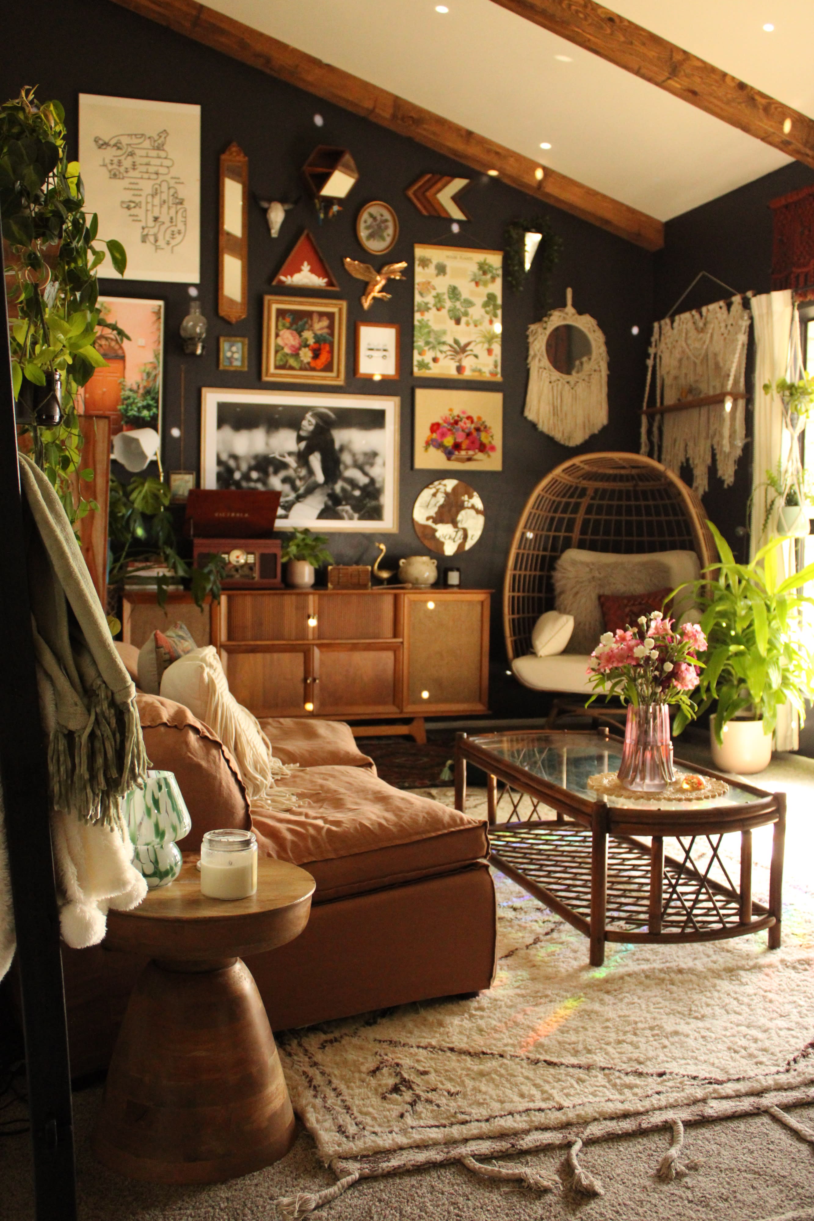 A woman examines a wedding dress hanging by the window in a decorated room filled with plants and wall art.