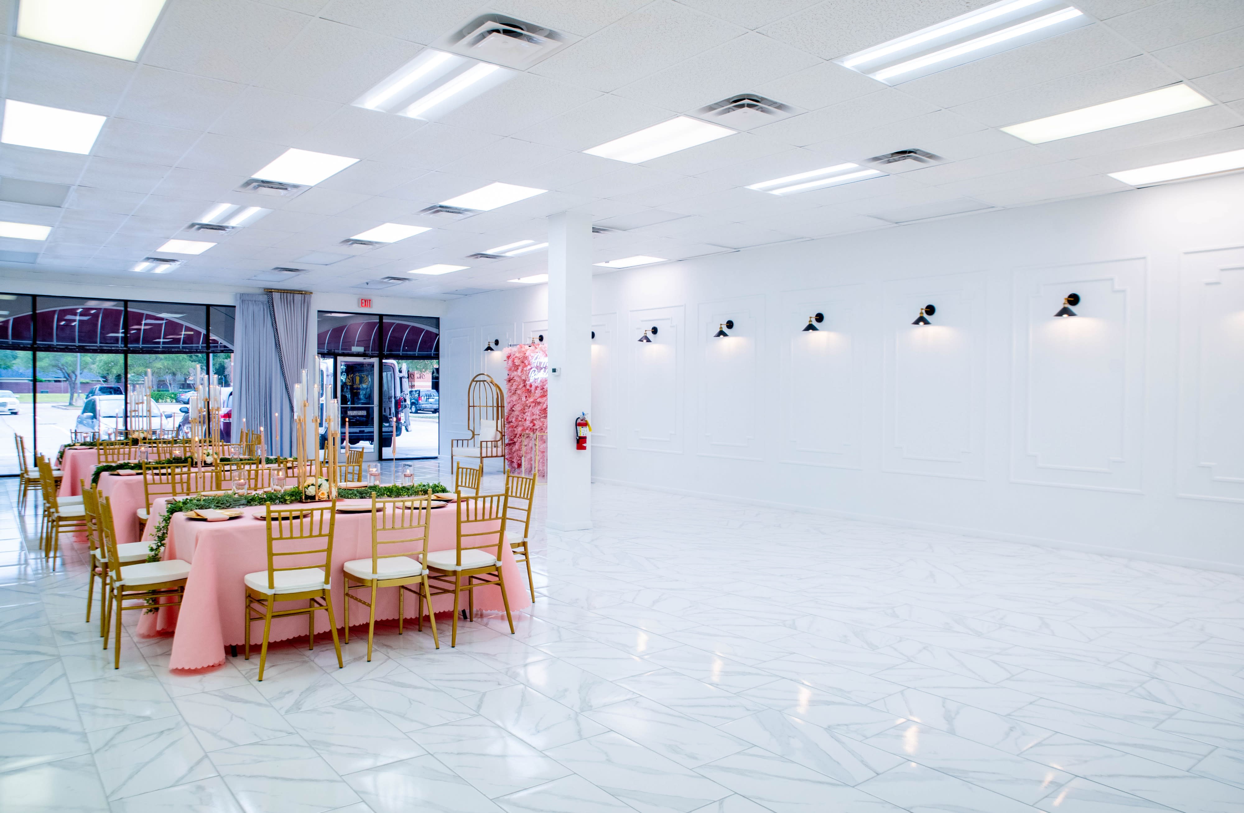 The venue is set up for a baby shower, featuring tables with pink covers, gold chairs, and decorative balloons.