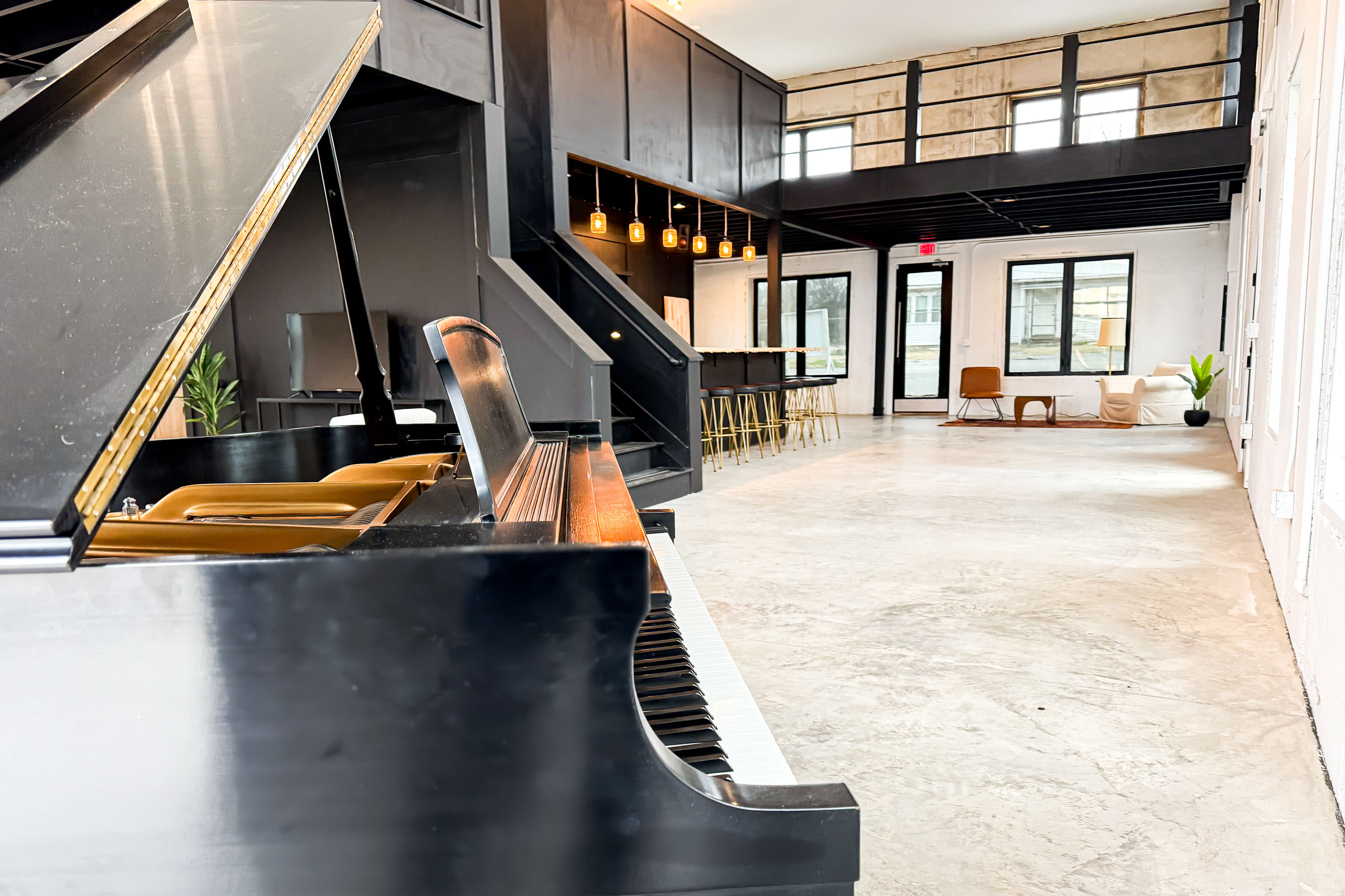 Two guests at a birthday dinner pose together, with one wearing a sparkling red dress and the other in a light gray suit, in a venue with large windows and a piano in the background.
