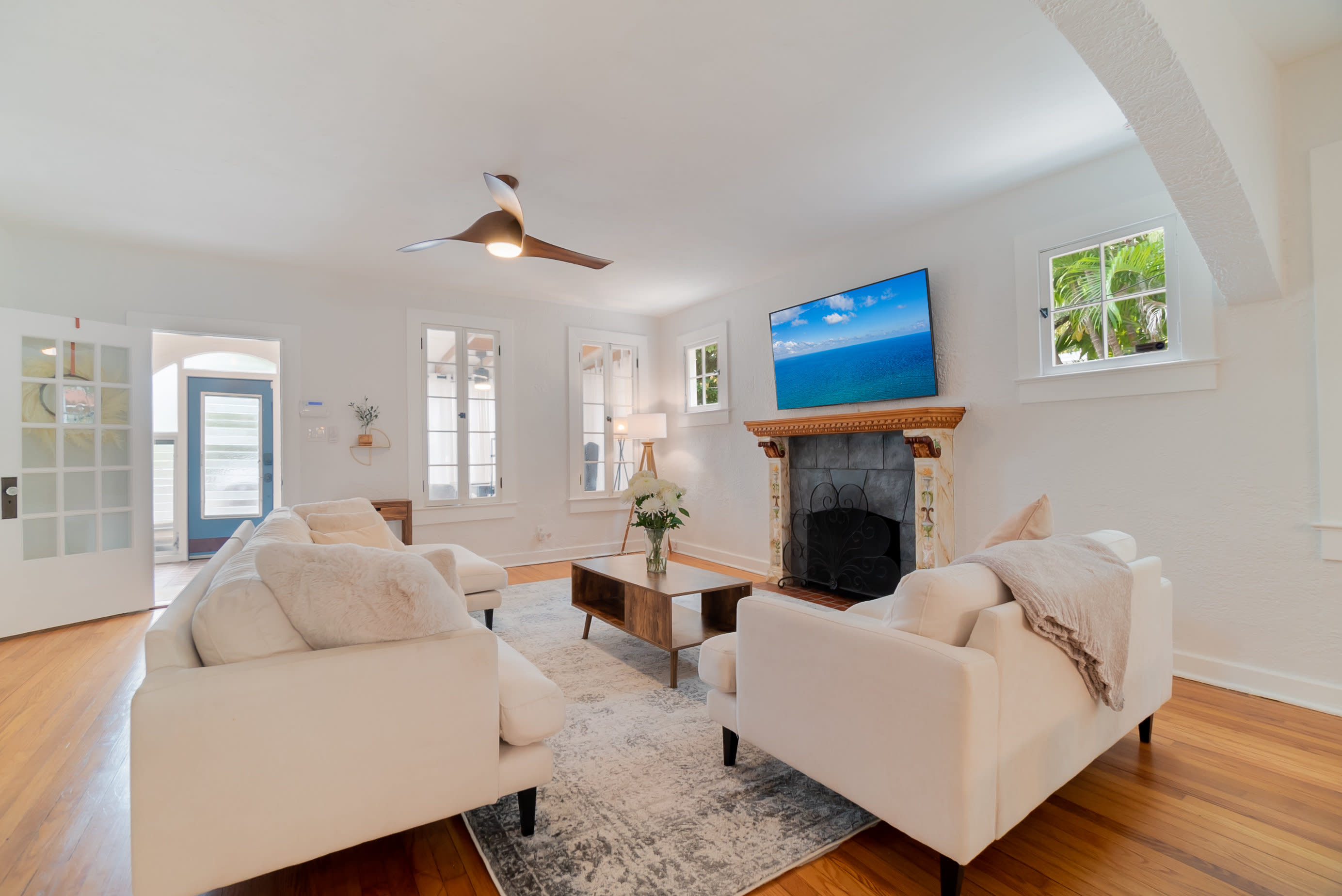 A modern living room features a white sectional sofa, a dark geometric coffee table, and a view of an adjoining kitchen.