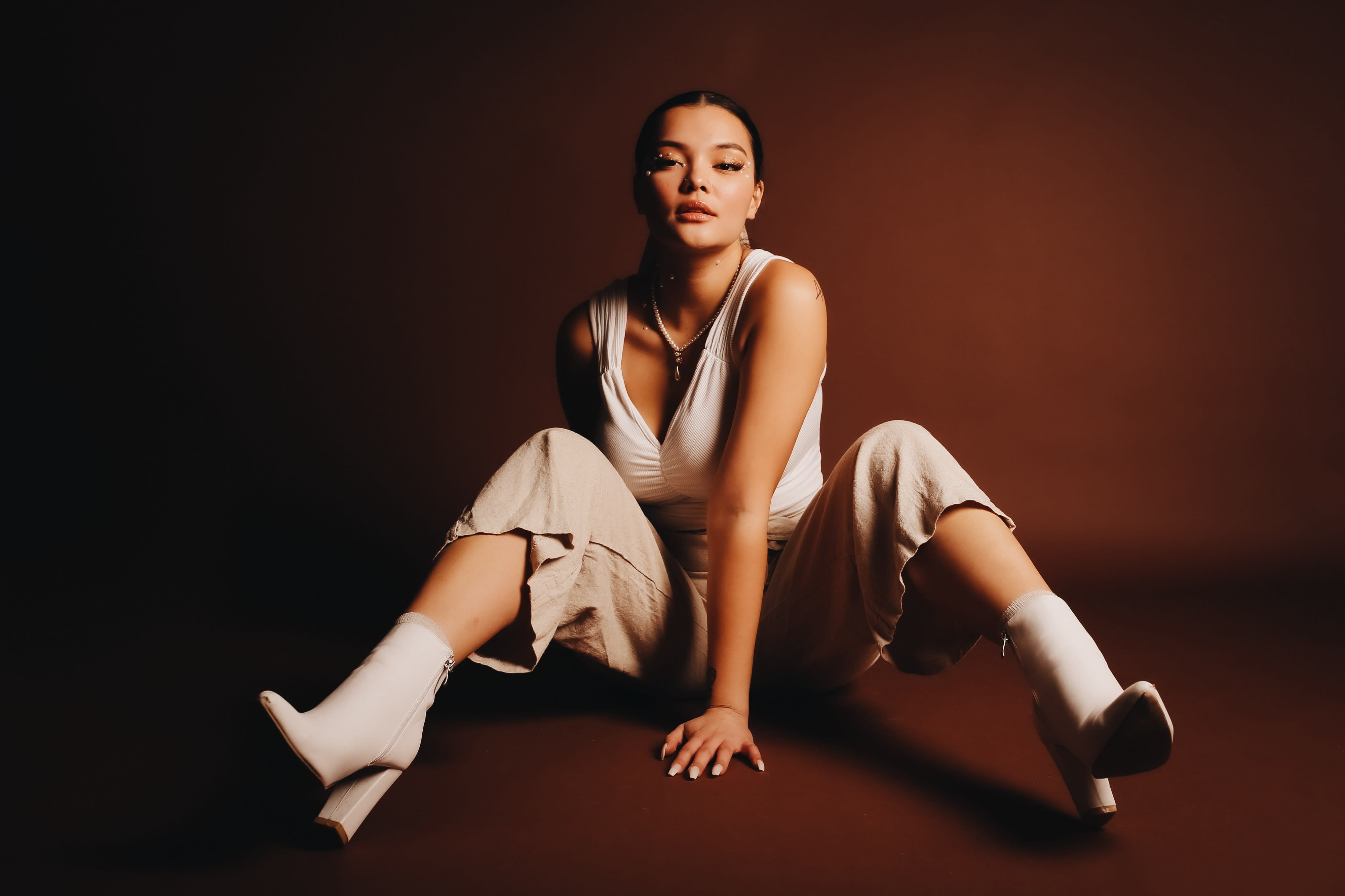 A woman is posing in a crouched position during a photoshoot, wearing athletic attire and adjusting her hair.