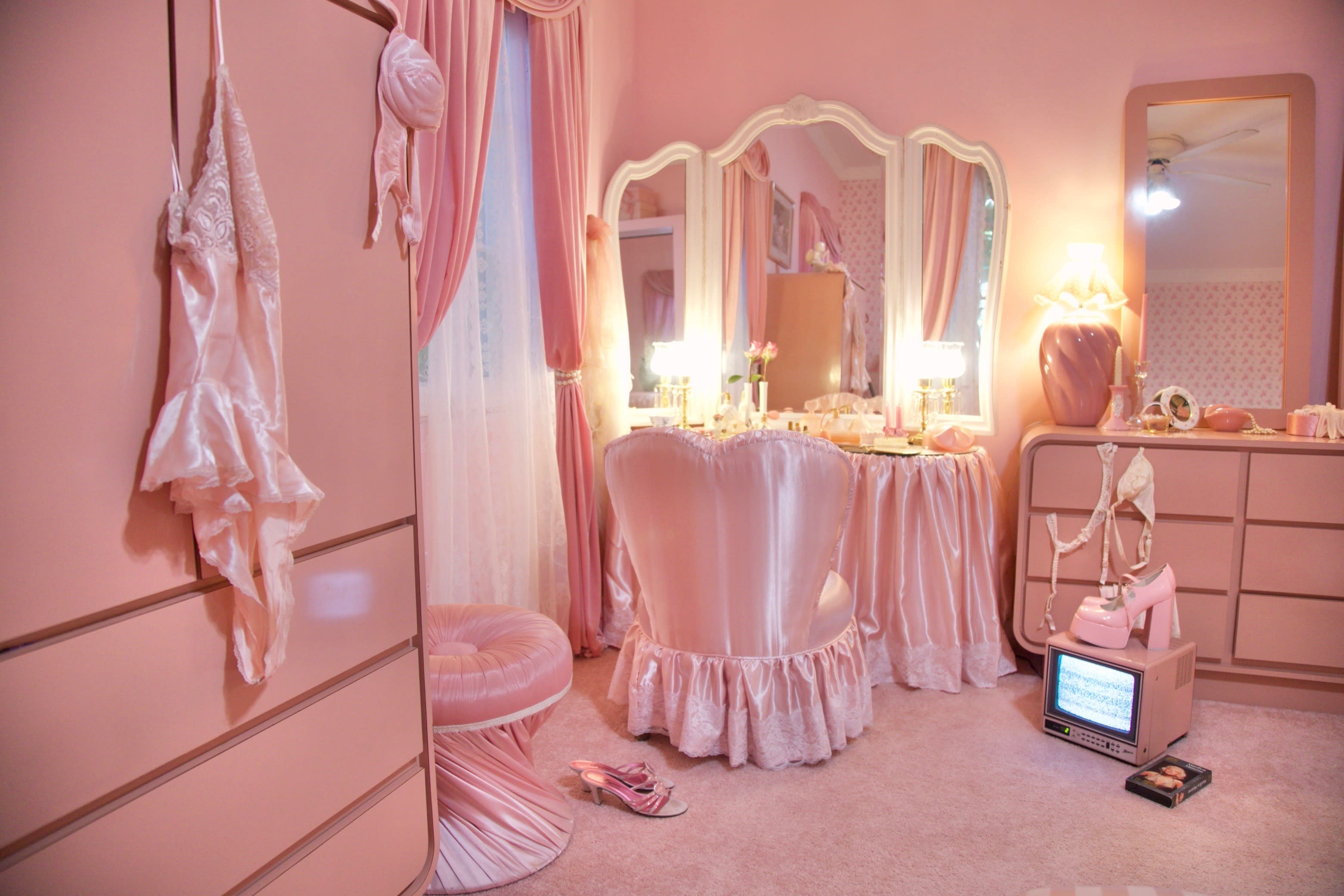A model in a pink dress sits in a cozy room decorated with a Christmas tree and pastel-colored gifts.