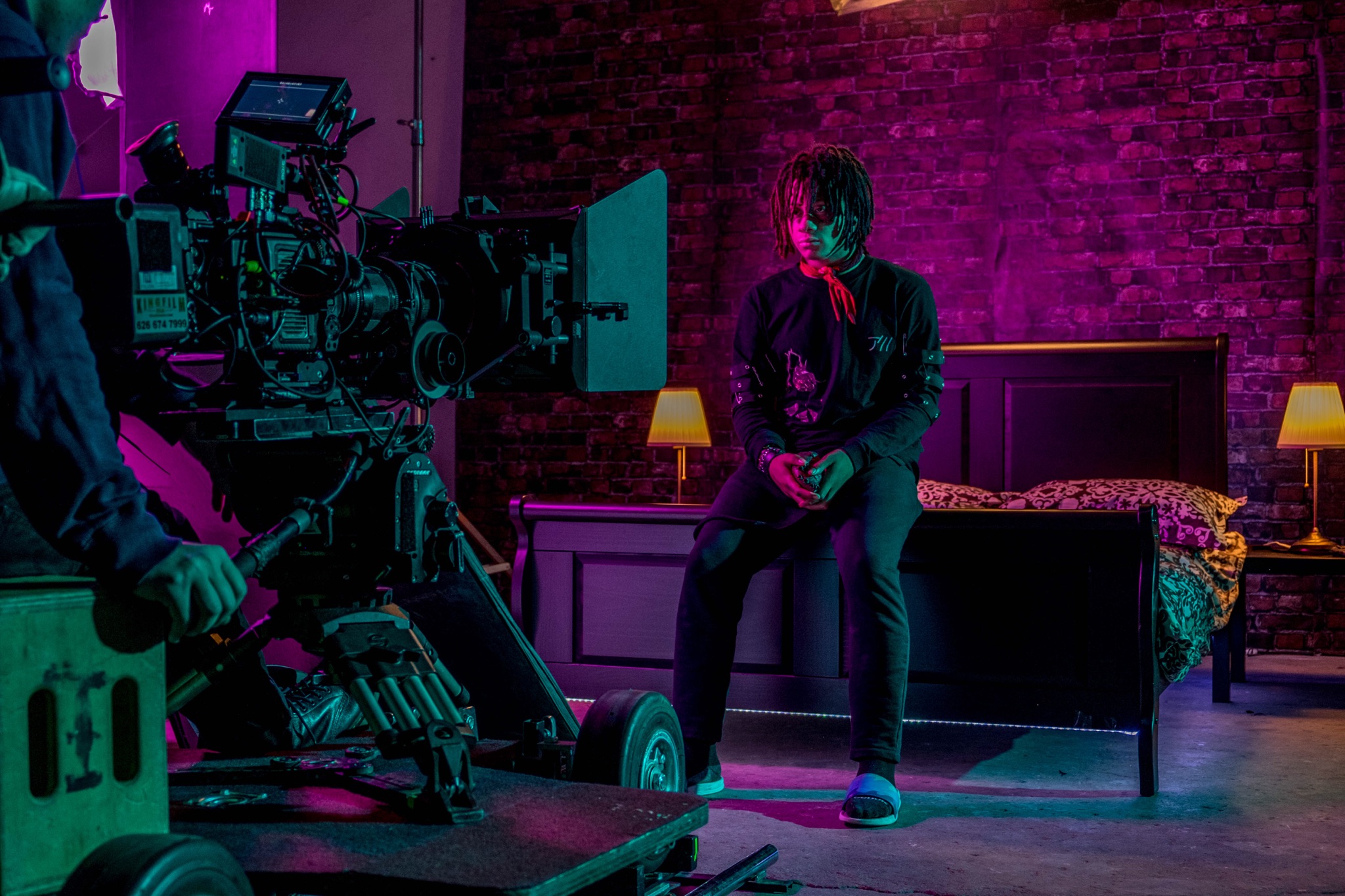A man in tactical gear sits against a warehouse wall, exuding a serious demeanor during a film shoot.