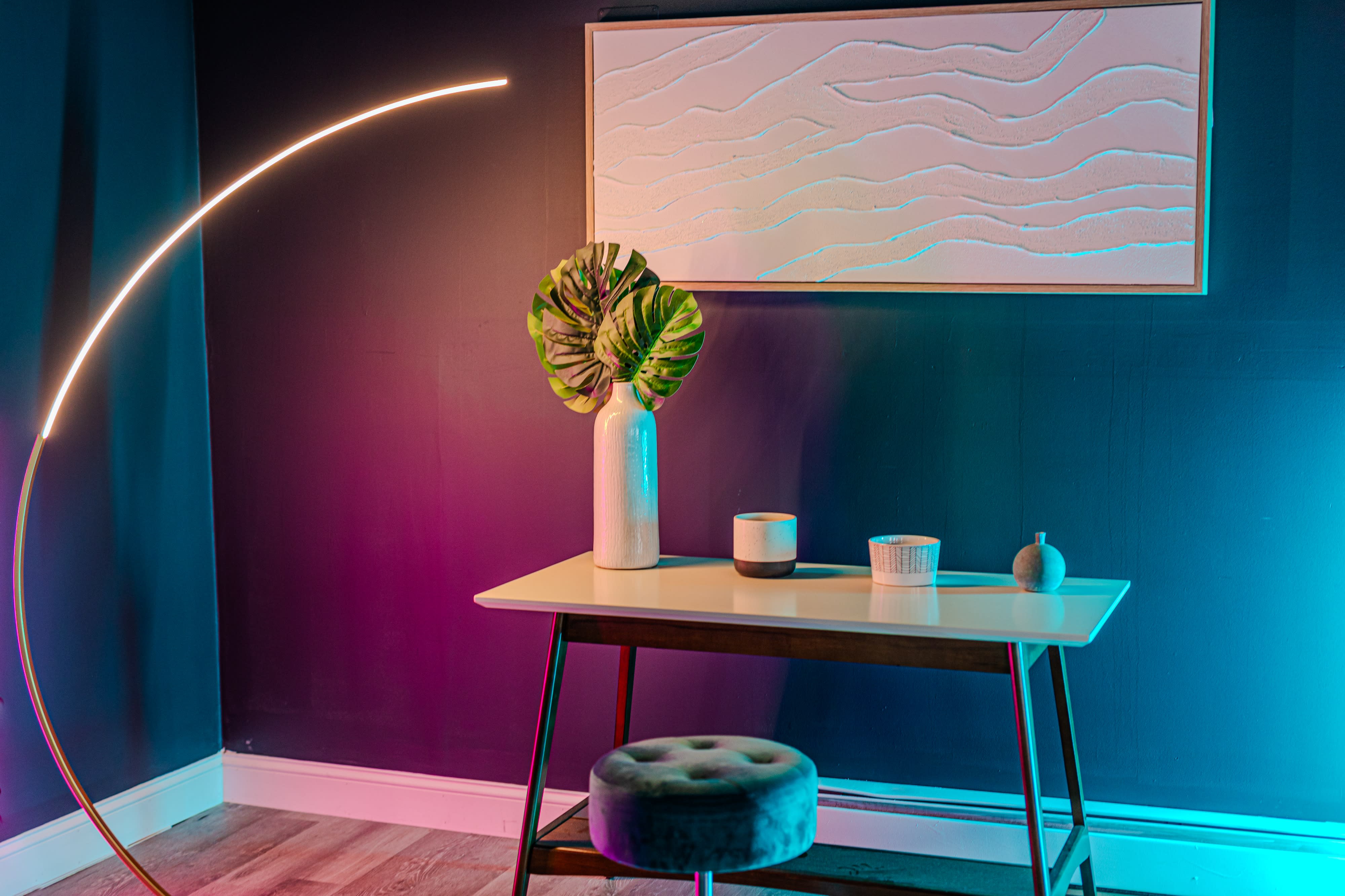 A person performs a high kick in a well-lit room furnished with a rug, chairs, and tables during a video shoot.