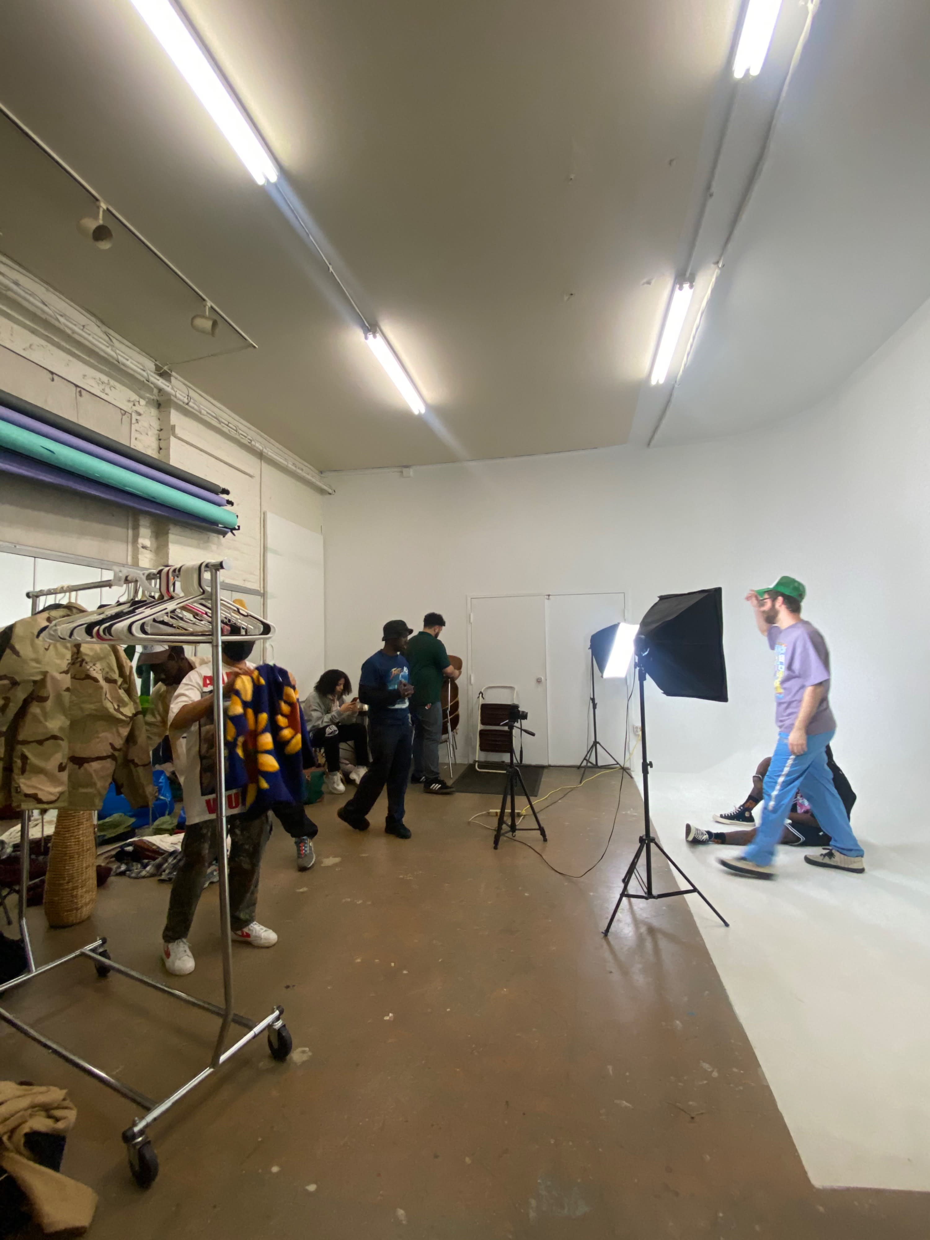 A group of five individuals poses in a studio, with four standing and one seated on a stool, while engaged in a photoshoot.