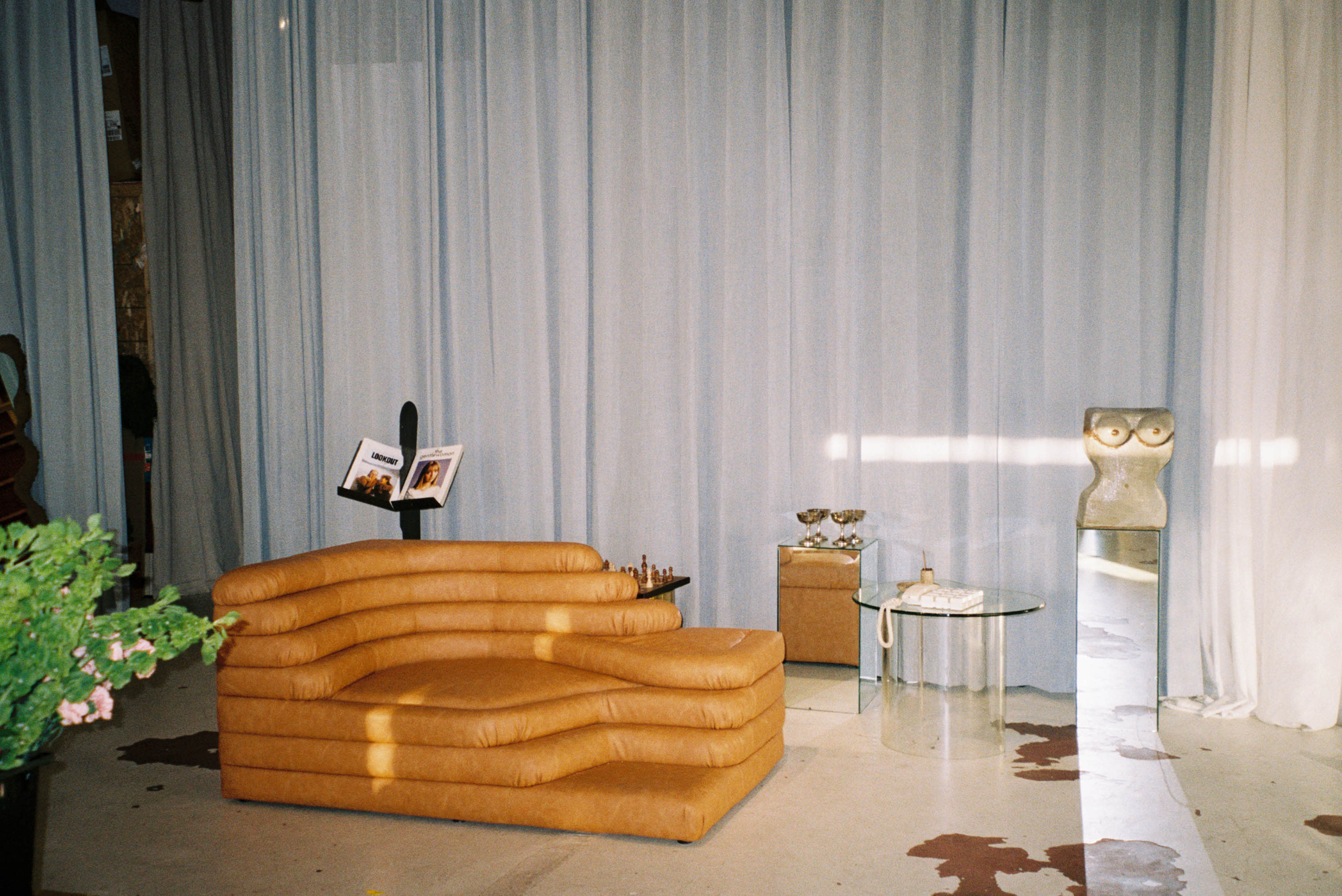 A person sits on a red sofa in a brightly lit room decorated with colorful books and ambient lighting while surrounded by various production equipment.