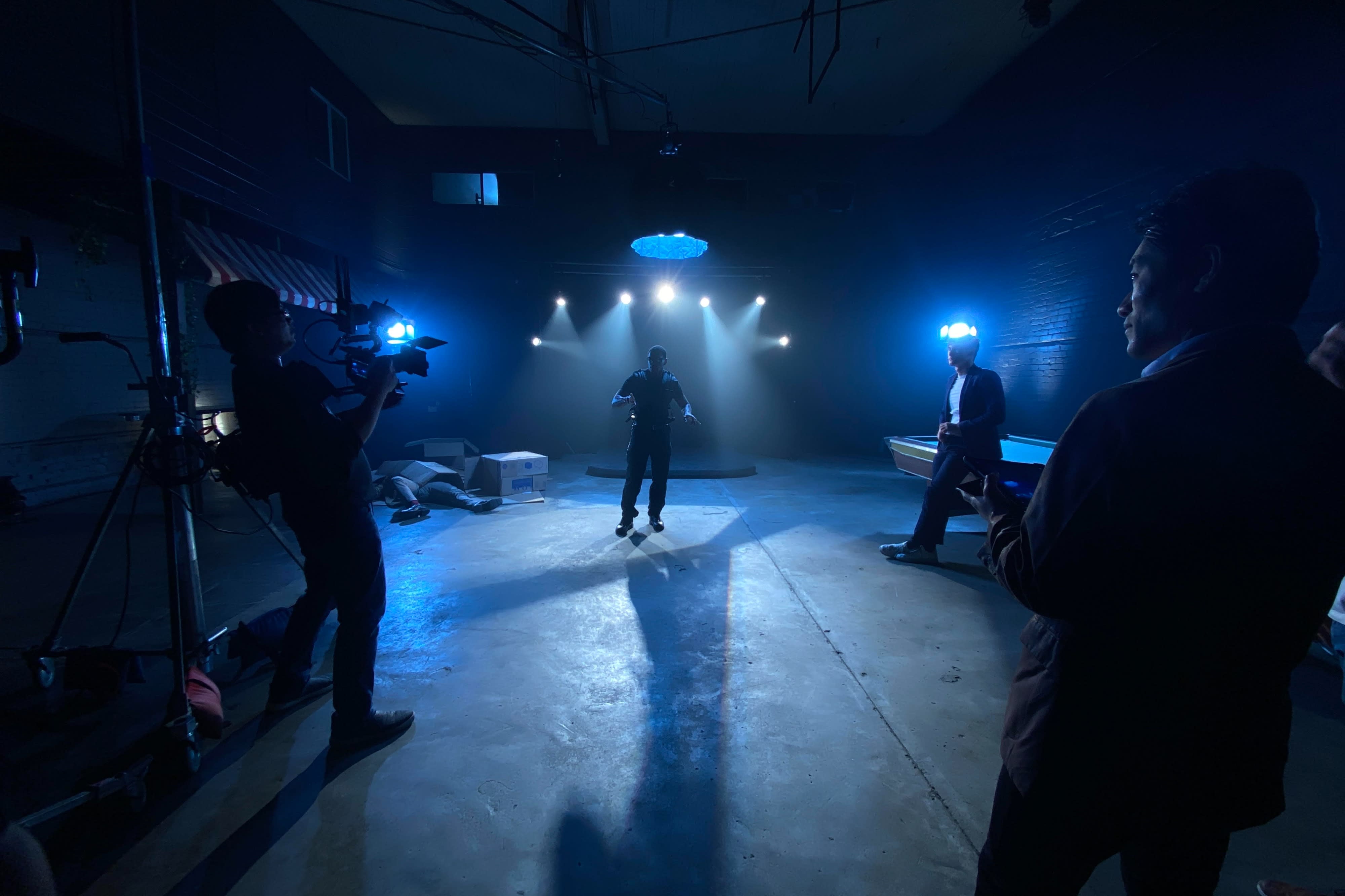 A musician plays guitar in a smoke-filled studio while a photographer captures the performance.