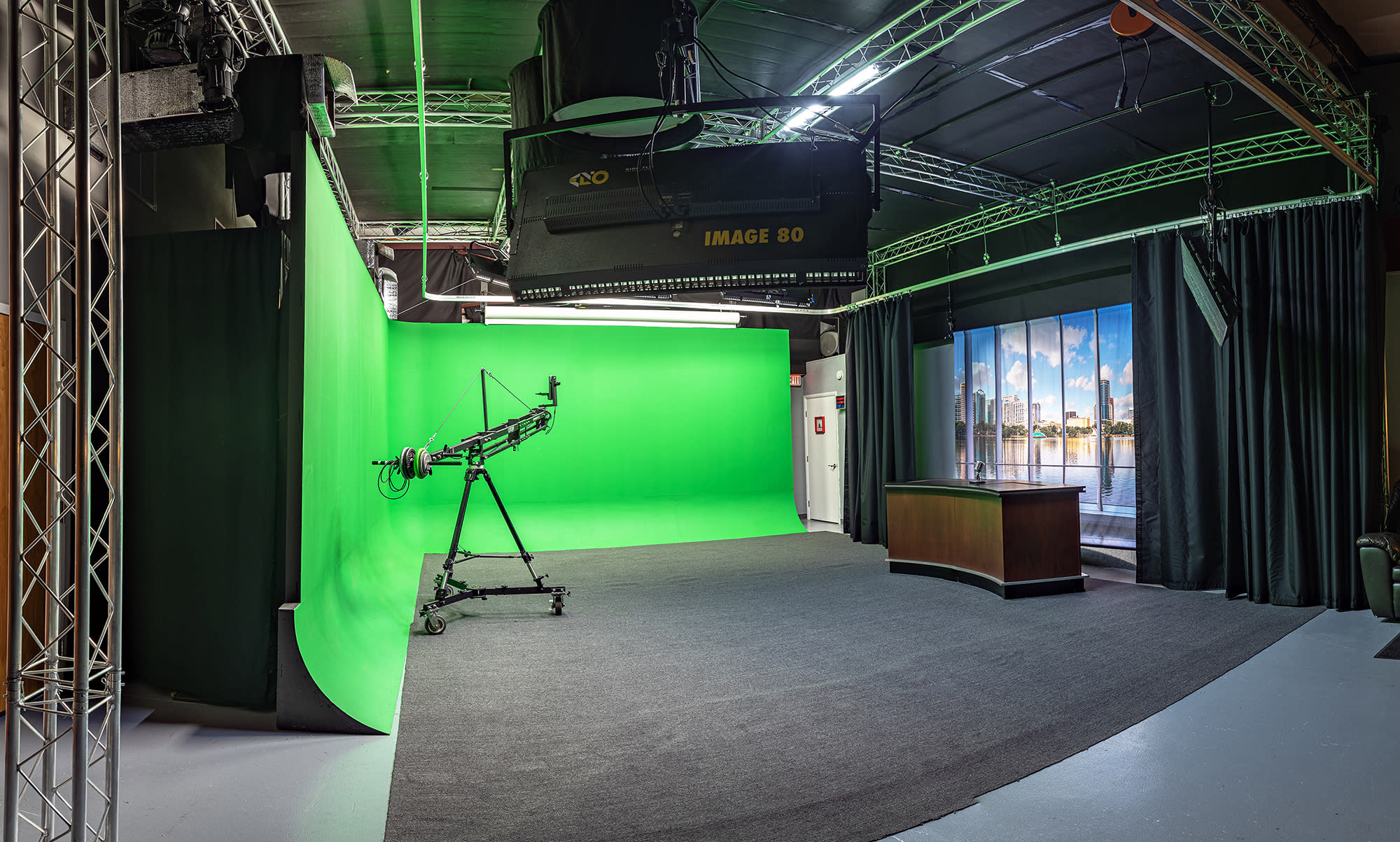 Two presenters stand at a black table in front of a green screen, preparing for a film shoot.