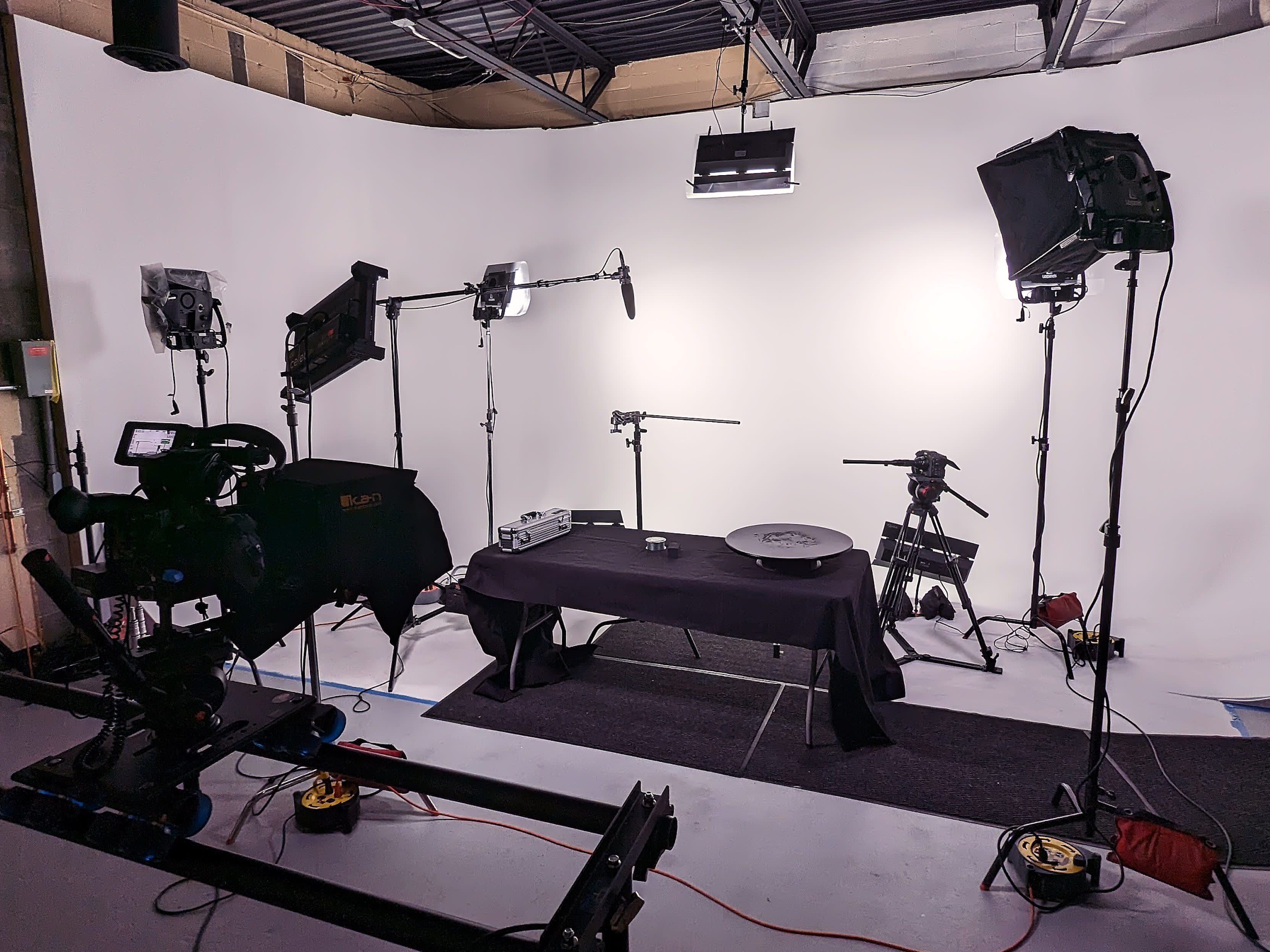 Two men sit on stools in front of a camera setup, surrounded by lighting and audio equipment for a video shoot.