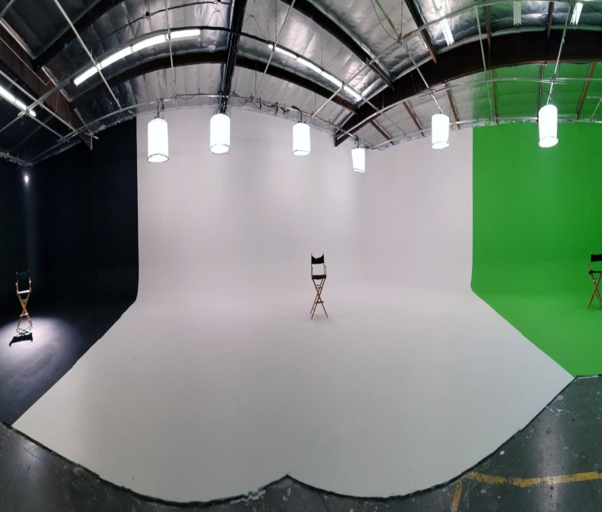 A child dressed as a superhero poses on a green backdrop while a crew member adjusts the camera during a video shoot.