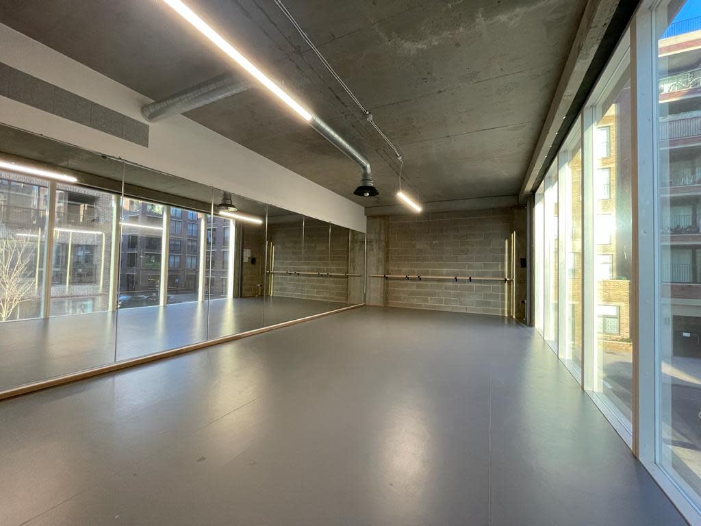 A woman performs a yoga pose while balancing on one hand in a studio with large windows.