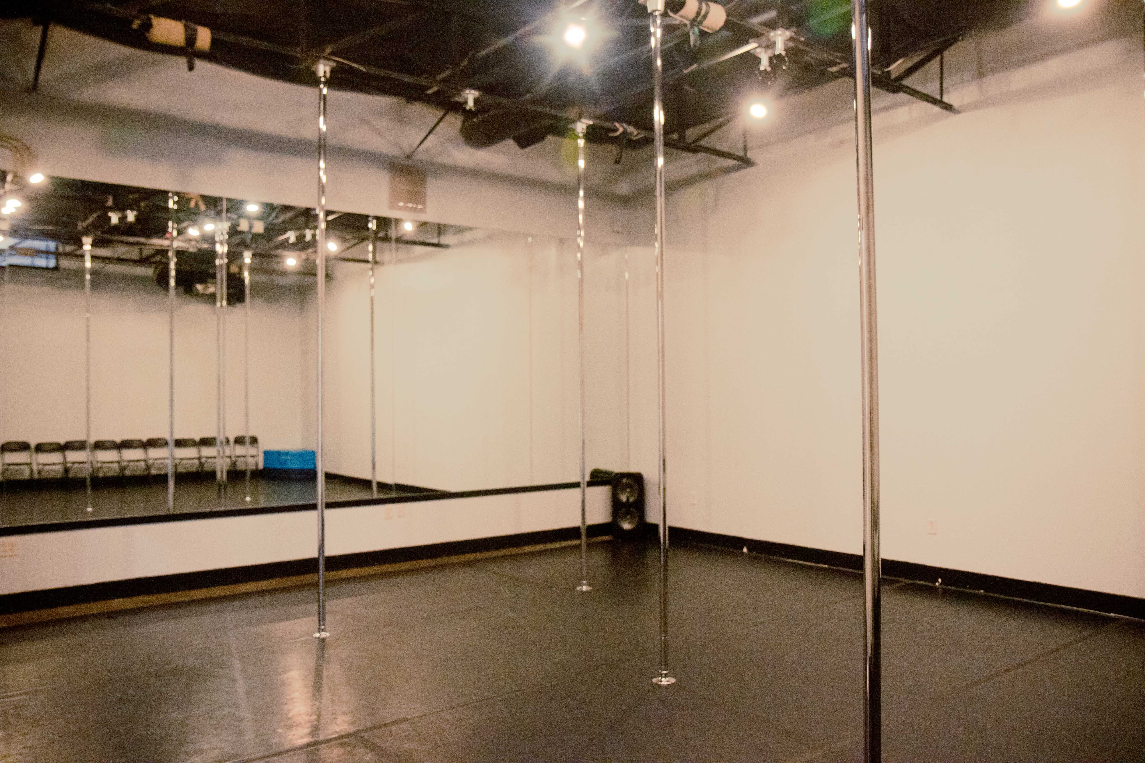 A group of seven women poses around a pole in a dance studio, showcasing their dance class environment.
