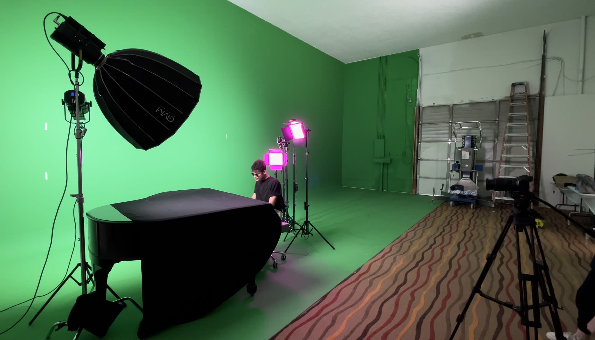 Two individuals prepare for a music video shoot in a studio setting, featuring a white car and multiple lighting setups.