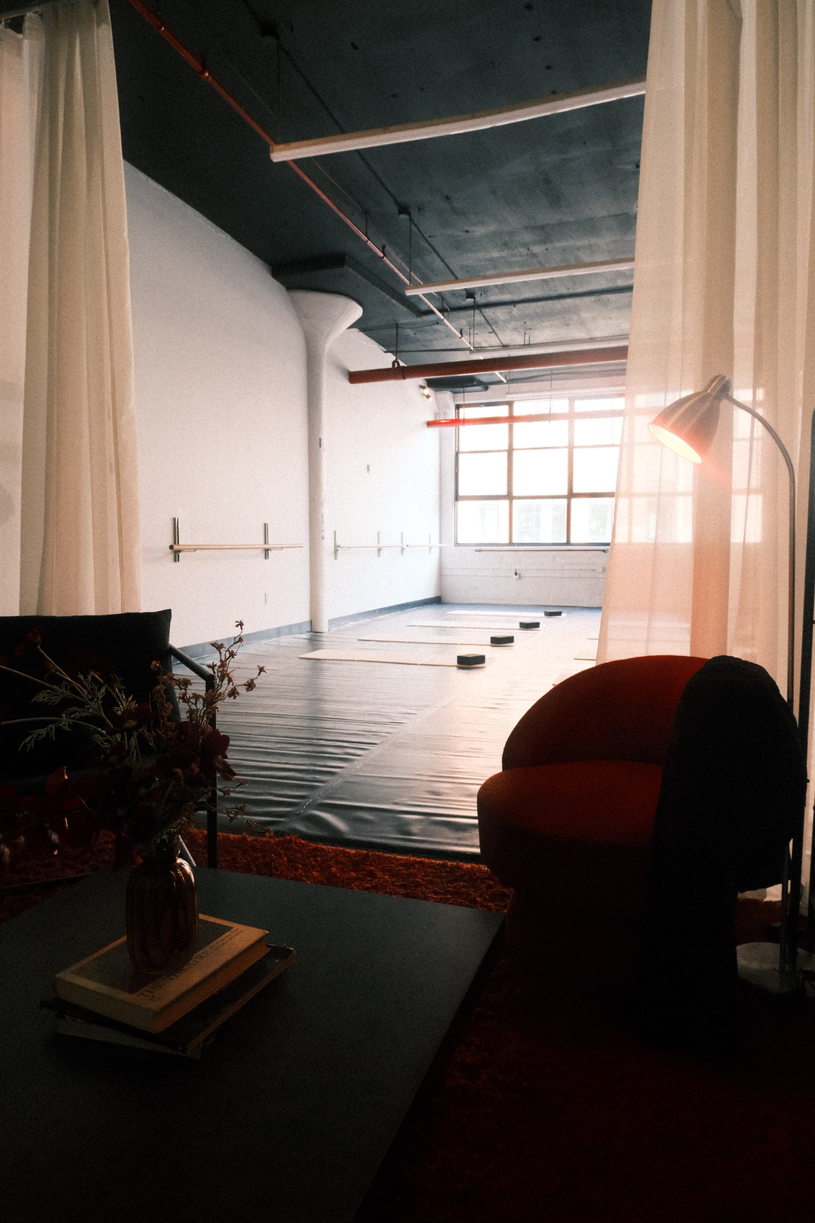 A group of individuals in a yoga class stretches on mats in a spacious studio with large windows.