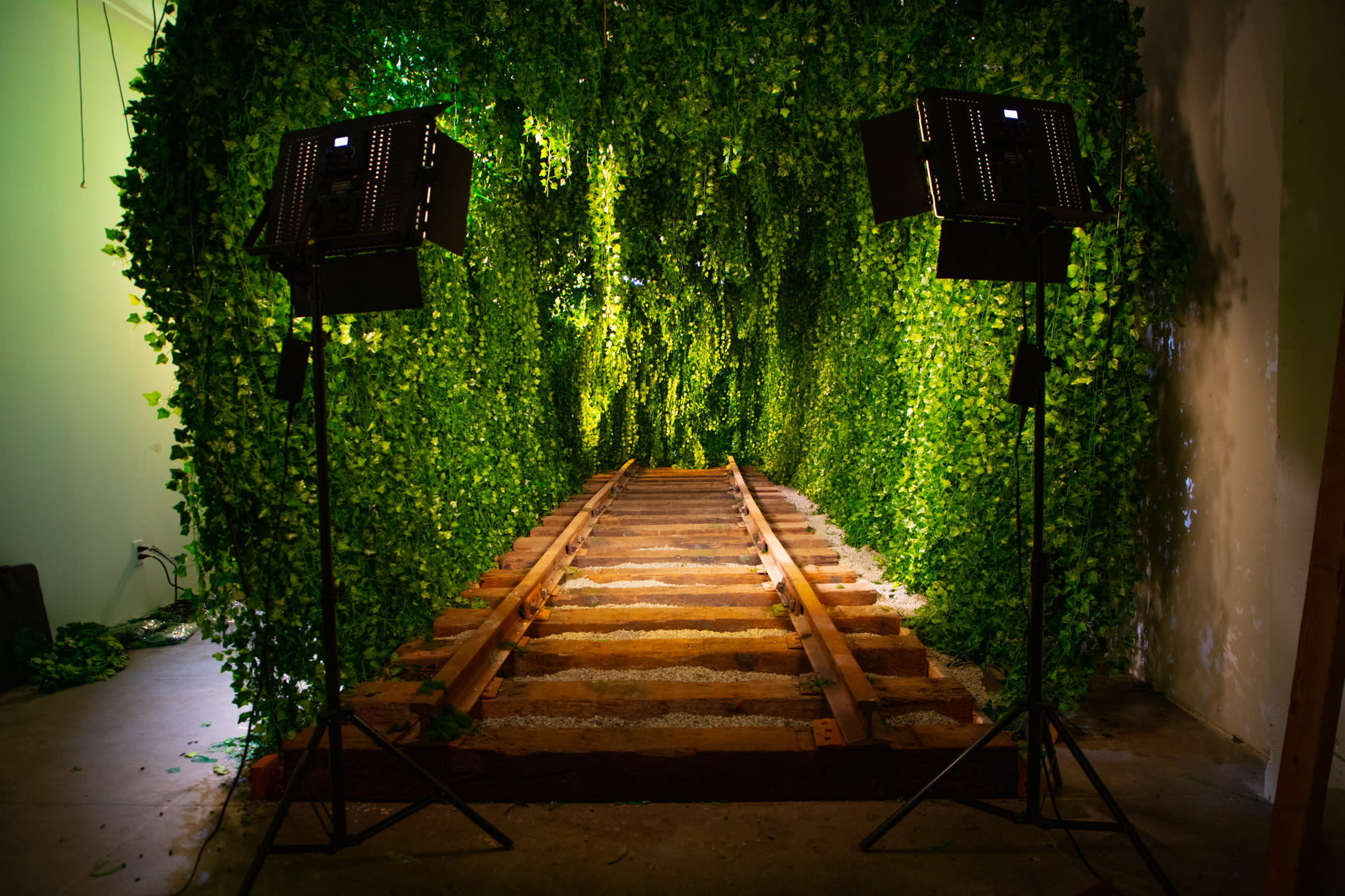 A model poses on wooden train tracks surrounded by a lush green foliage backdrop.