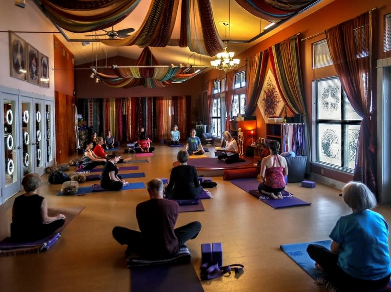 A group of participants lies on mats and cushions in a serene room, while an instructor facilitates a sound bath session with various instruments.