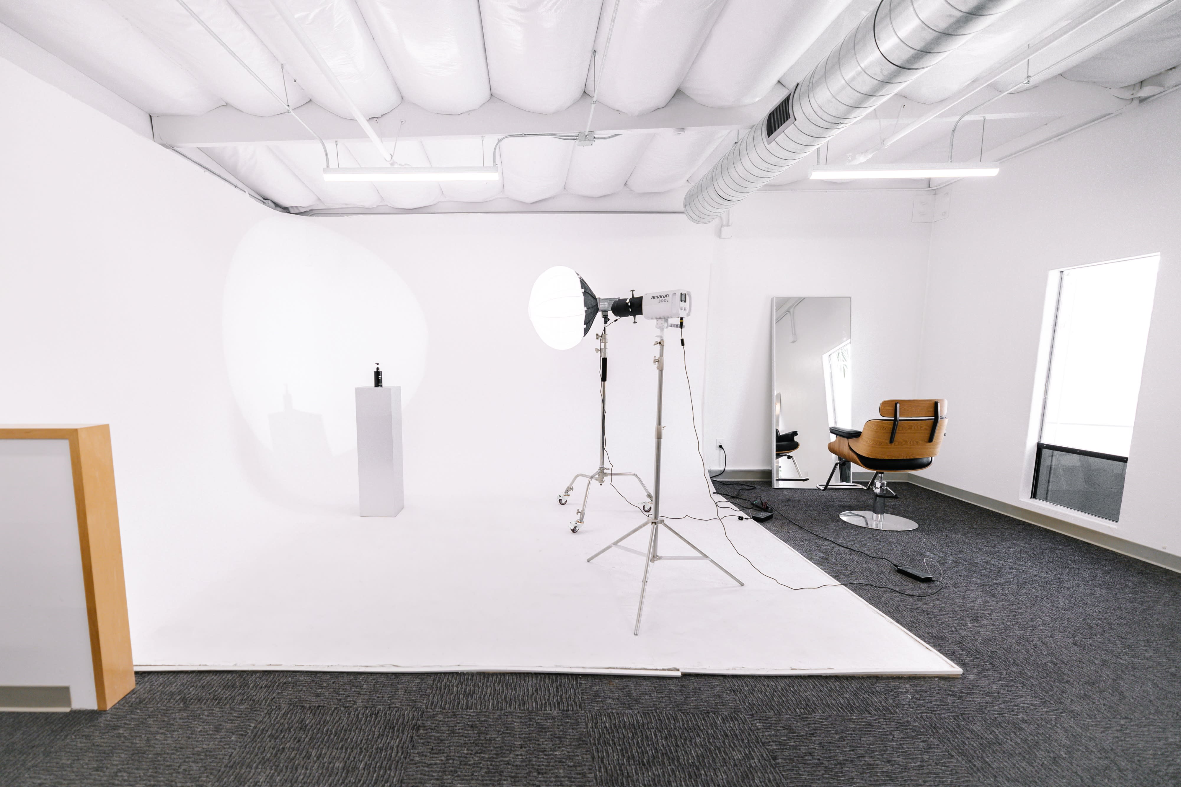 A photographer sets up a clothing brand photo shoot in a spacious studio with a plain white backdrop and professional lighting equipment.