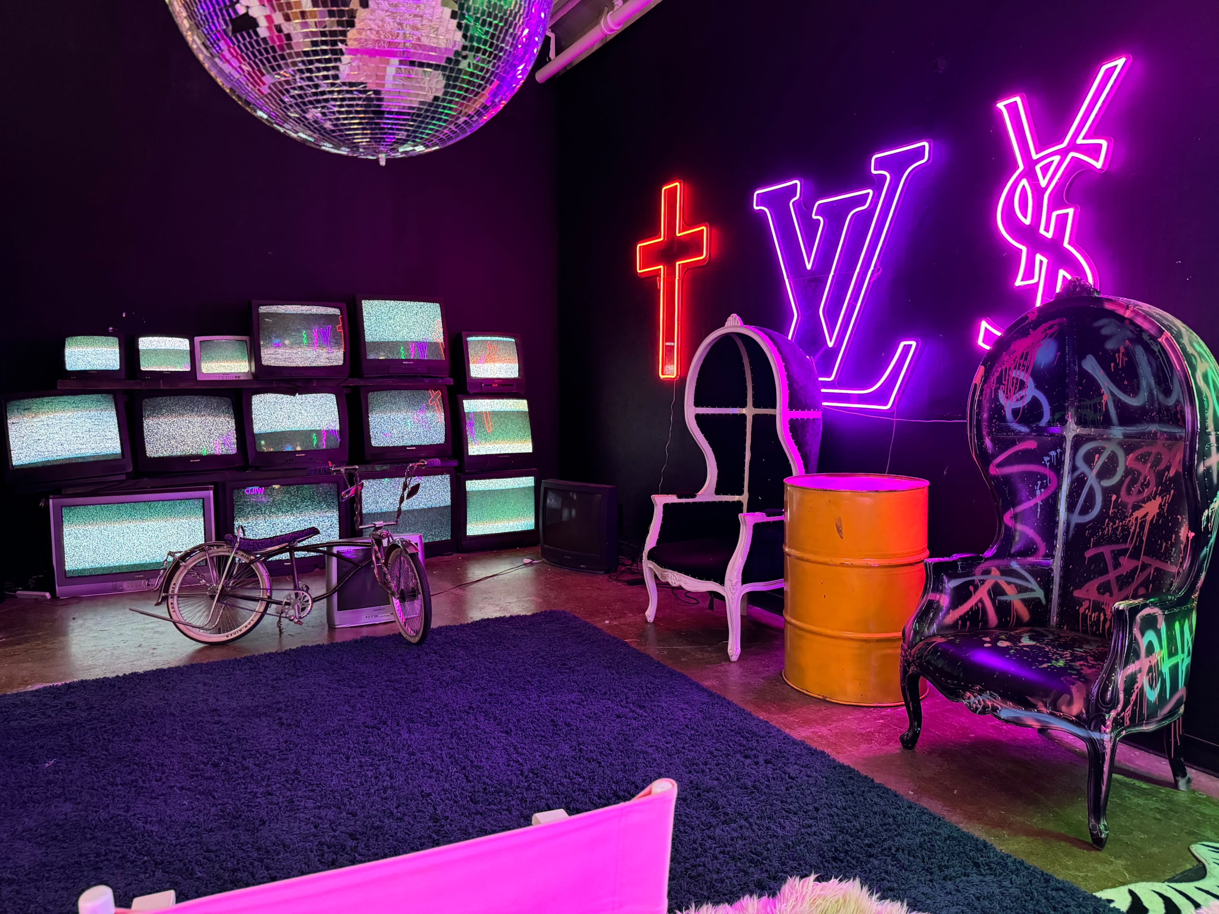 A group of seven young people poses casually in front of a wall of vintage television sets during a video shoot.