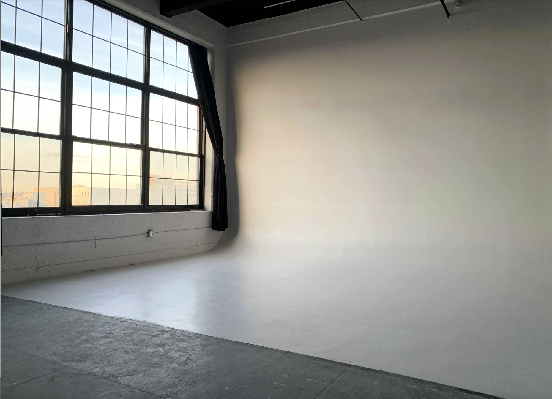 A model poses on a pedestal, holding two long braids that flow dramatically on either side of her in a minimalist studio setting.