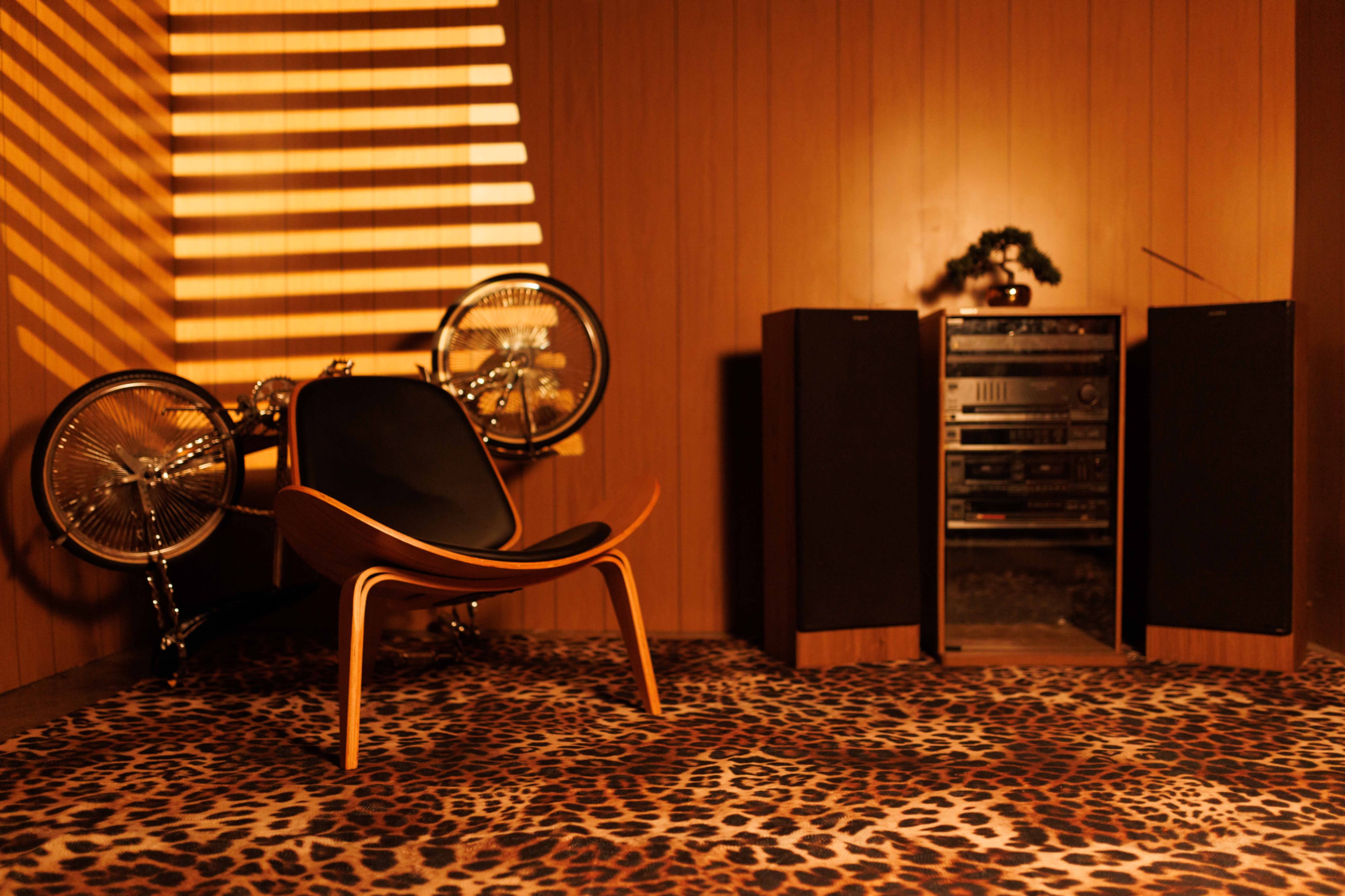 A group of musicians and performers is set up in a retro-styled room, preparing for a live performance on a brown sofa.