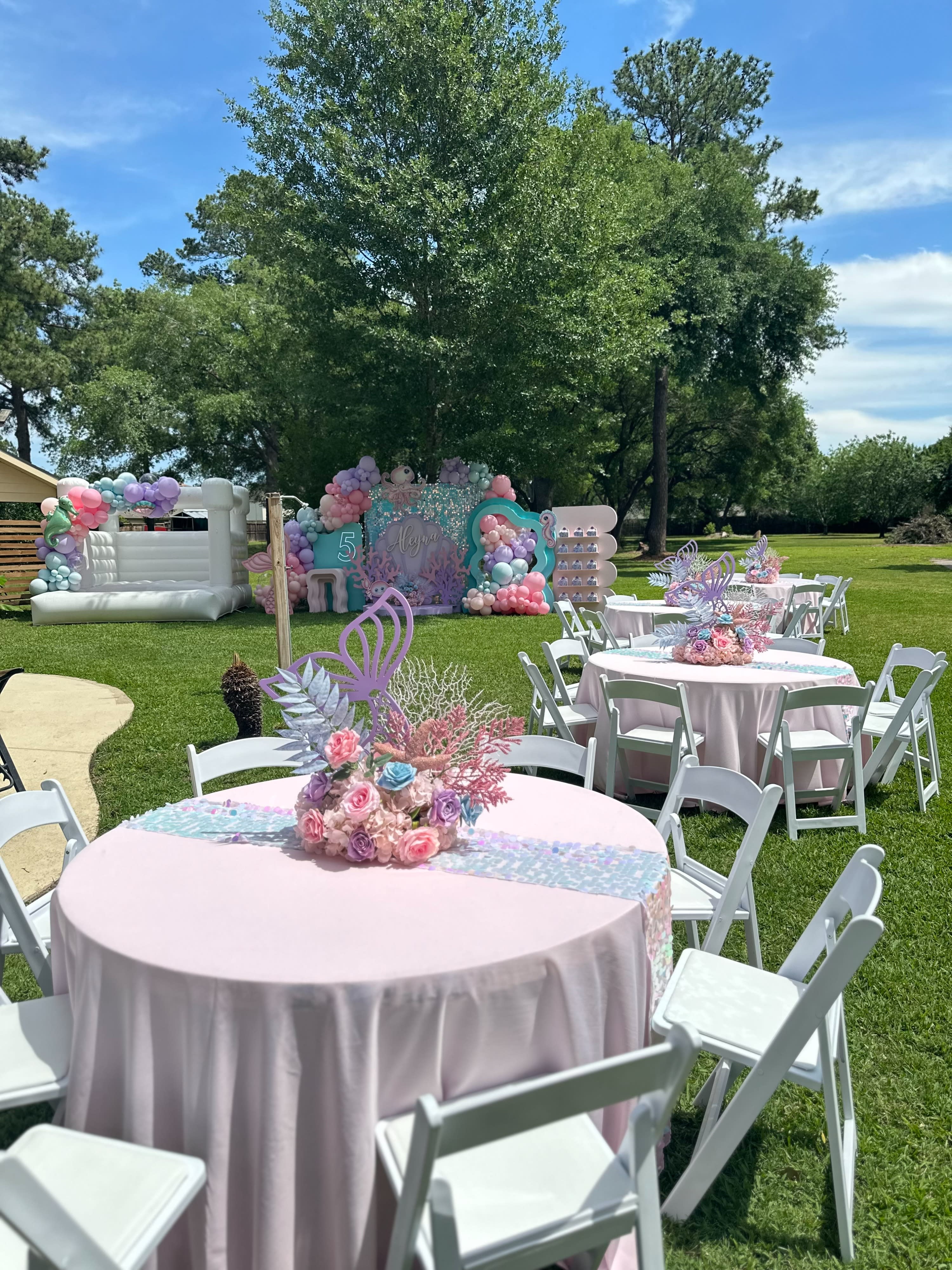 A large pink-themed bounce house is decorated with balloons and streamers, creating a festive space for children to play.