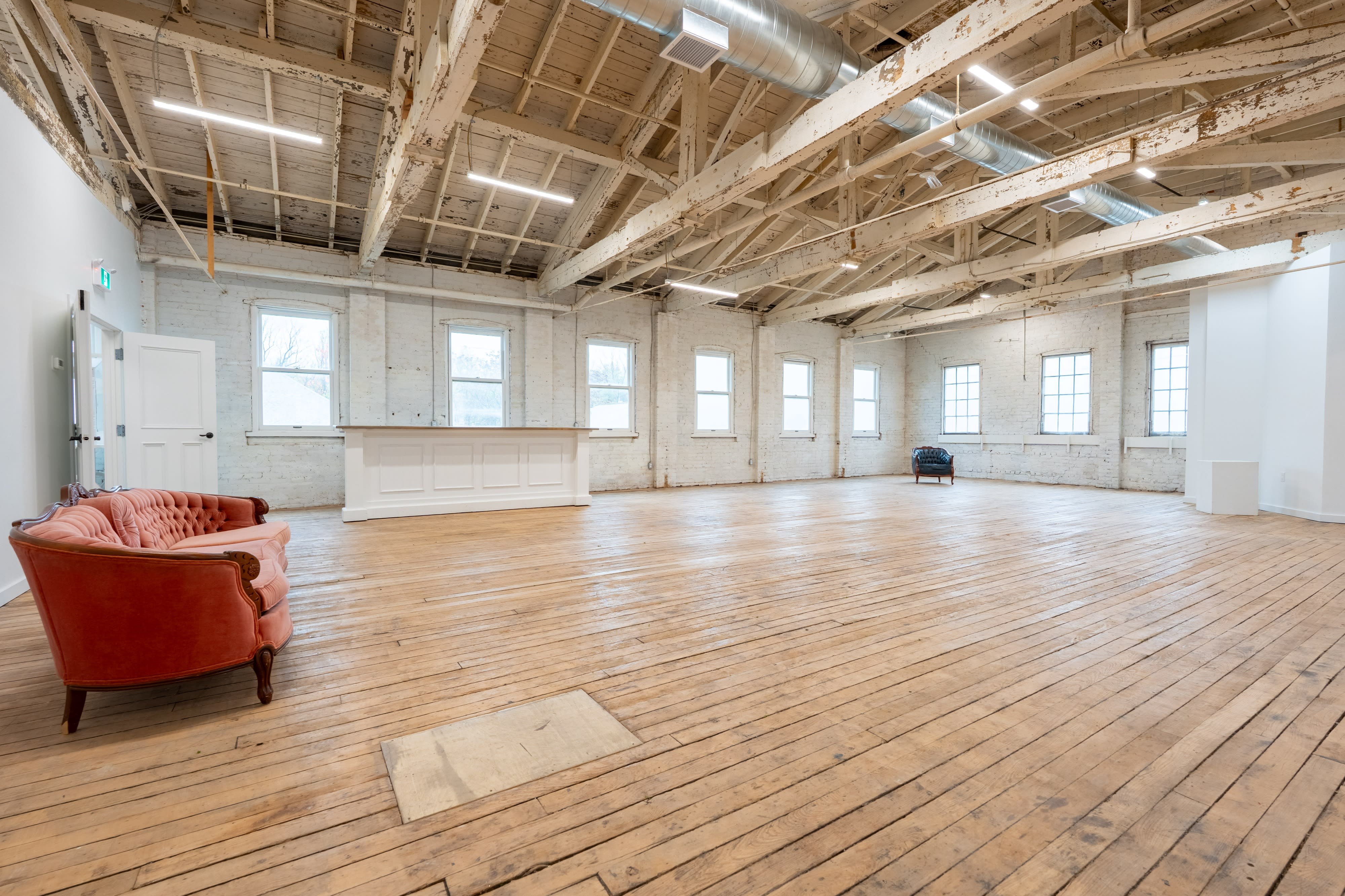 An artist is painting on an easel in a spacious studio with large windows and minimal decor.