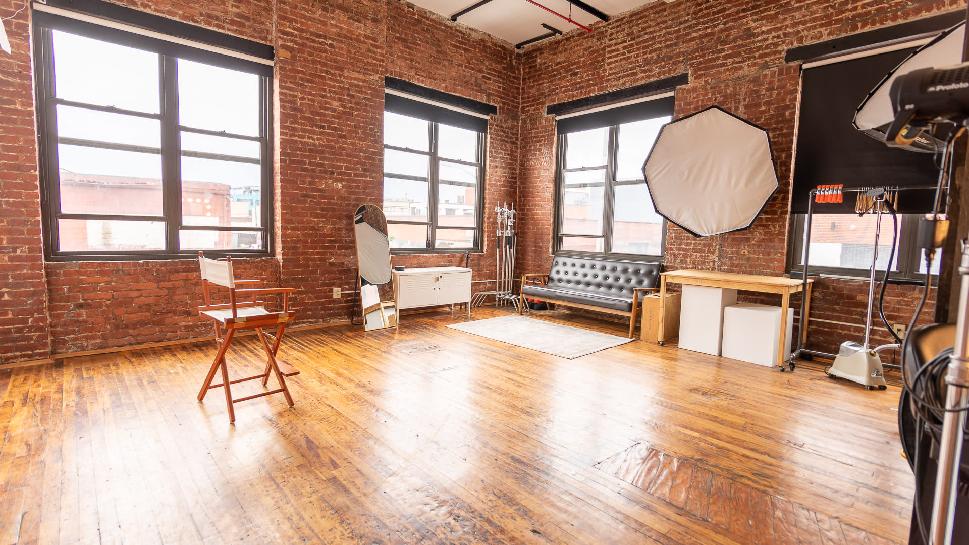A person sits on a stool in front of a backdrop while another person operates a camera during a photo shoot.