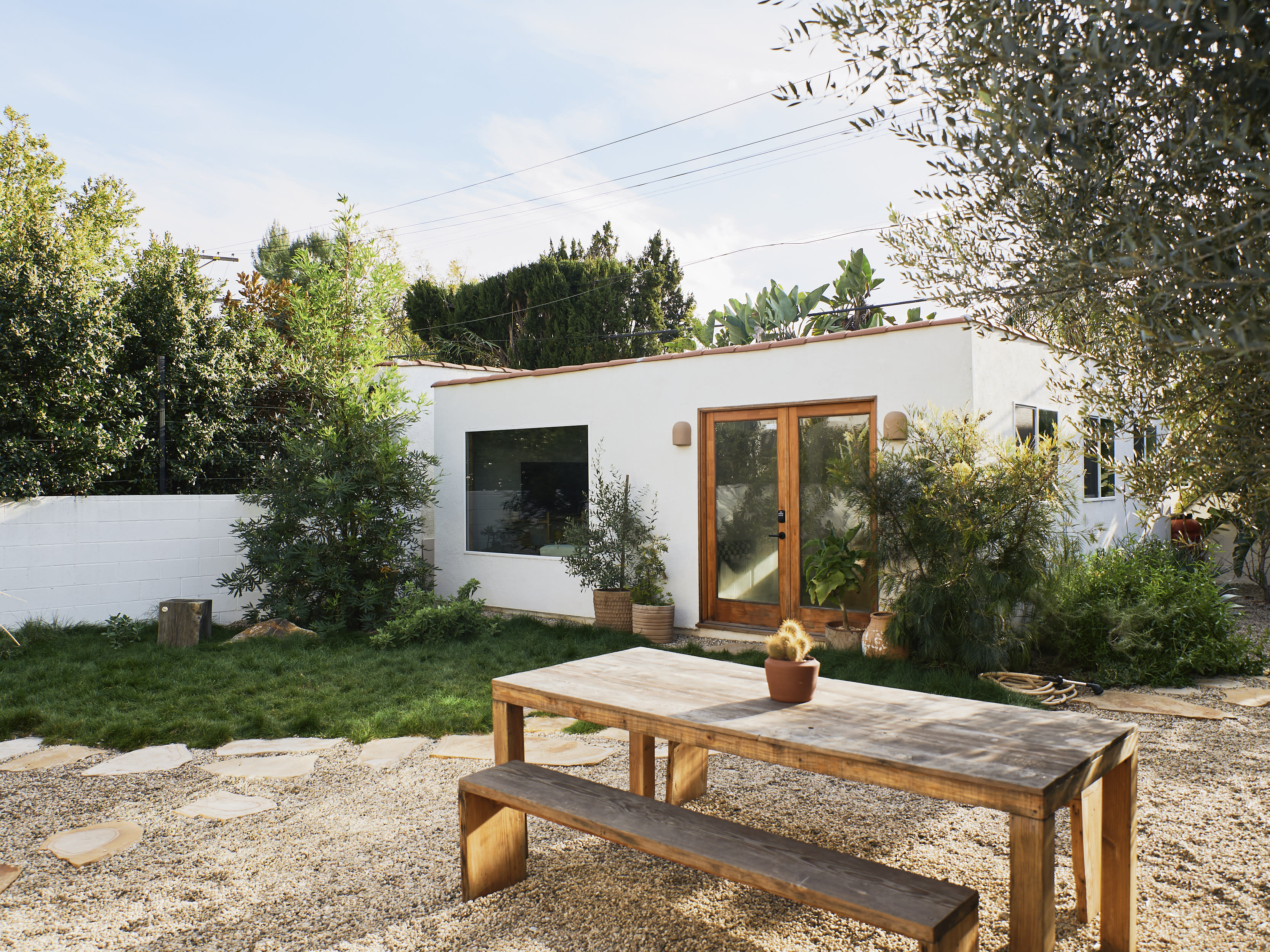 A group of four people enjoys a meal together at a beautifully set outdoor table surrounded by greenery.