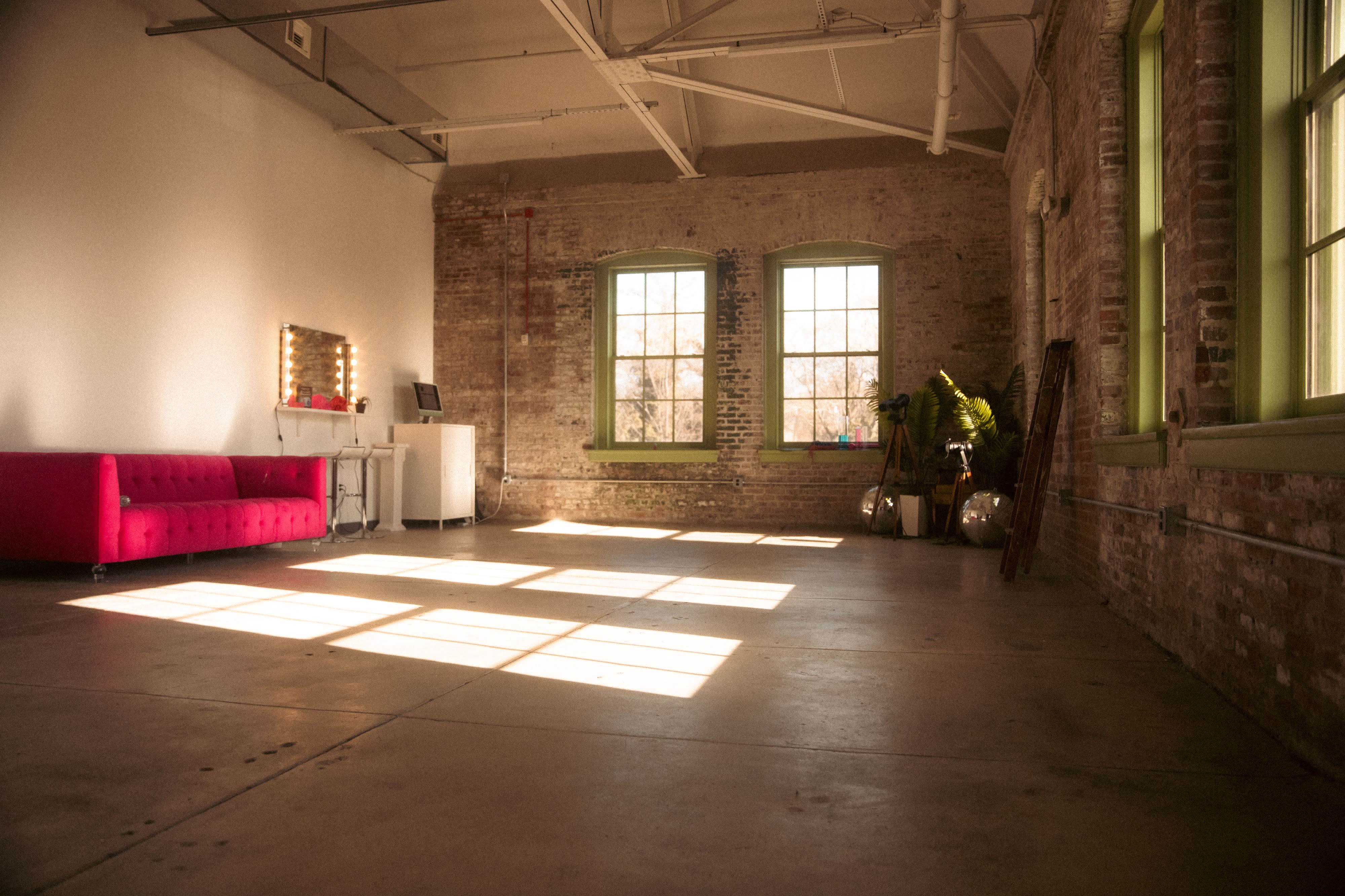 A video shoot is set up in a spacious room featuring multiple cameras and lighting equipment around a vibrant pink couch.
