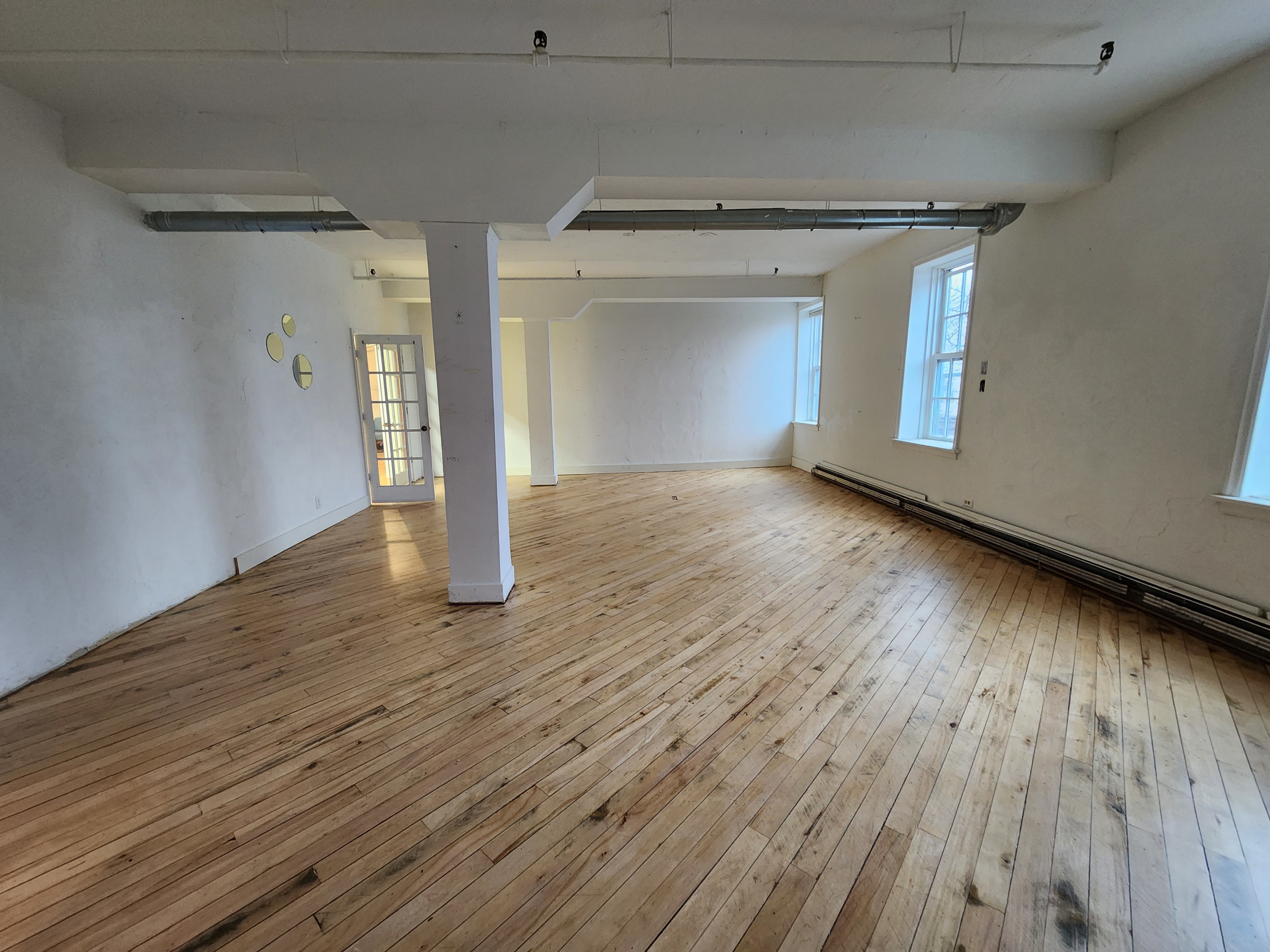 A bright, empty studio space features wooden floors, a decorative rug, and overhead string lights.