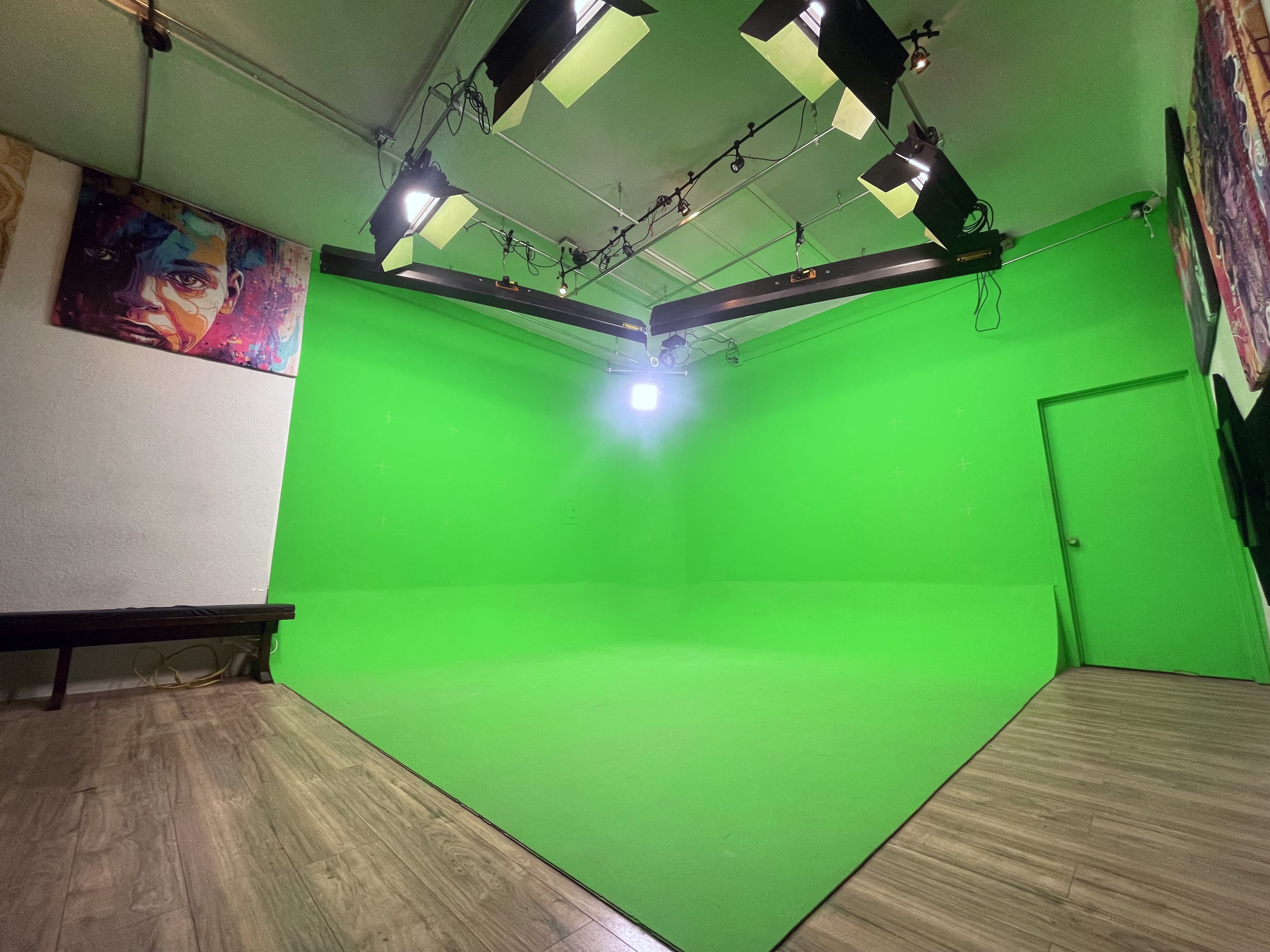 A man in a gnome costume sits on a box, holding a hammer in front of a green screen during a video shoot.