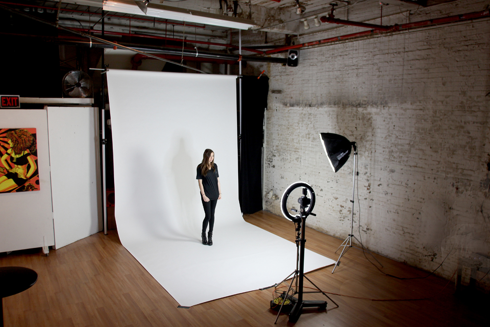 A model is captured mid-air, striking a dynamic pose while wearing a black outfit against a plain backdrop.