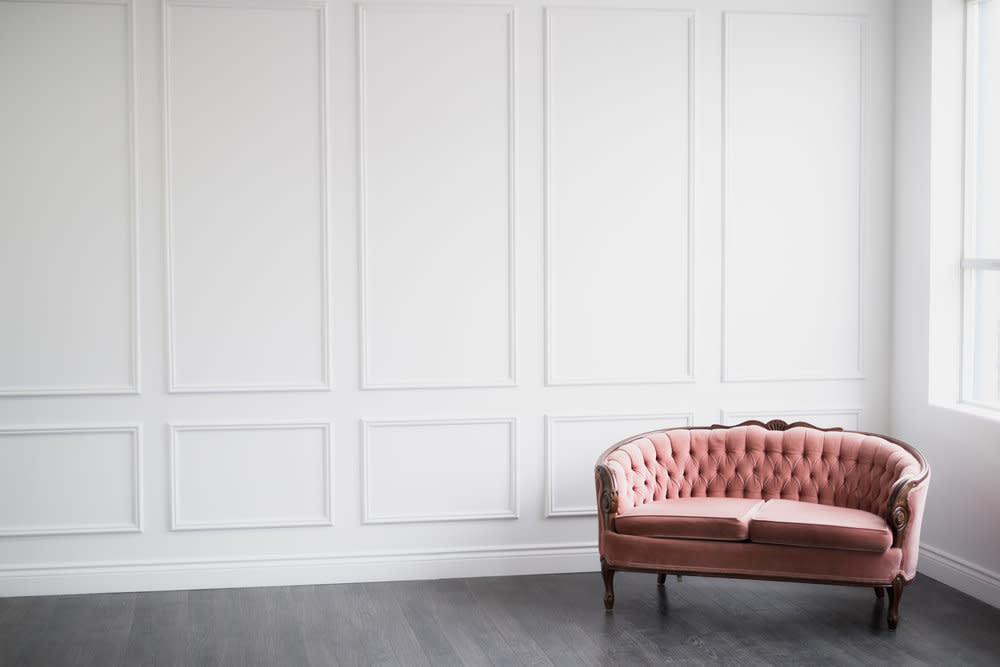 A woman sits beside a canvas depicting ocean waves, holding a paintbrush, in a bright room with a white brick wall.