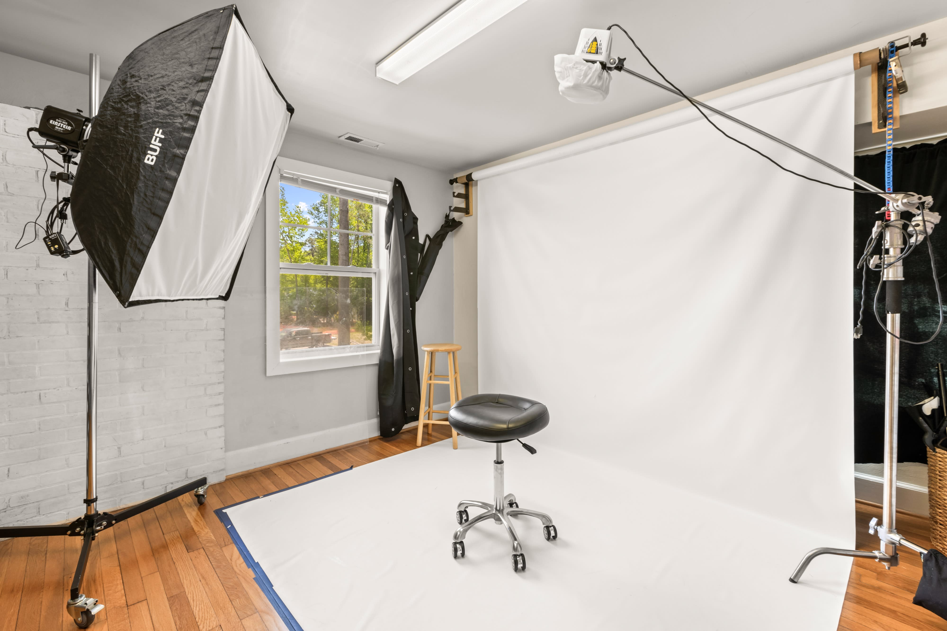 A model poses on a bed, dressed in a black outfit, while a photographer takes pictures from a distance.