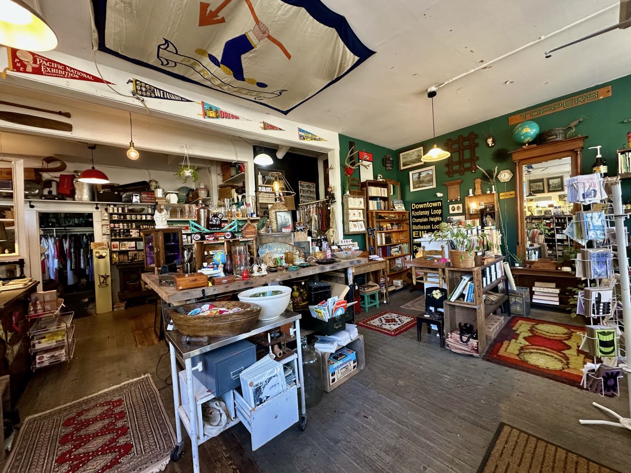 A duo poses for a photoshoot in a vintage store, showcasing their outfits and accessories amidst shelves filled with colorful items.