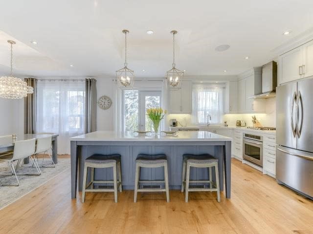 A decorative vase filled with pampas grass sits on a wooden tray in the center of a bright kitchen, illuminated by hanging light fixtures.
