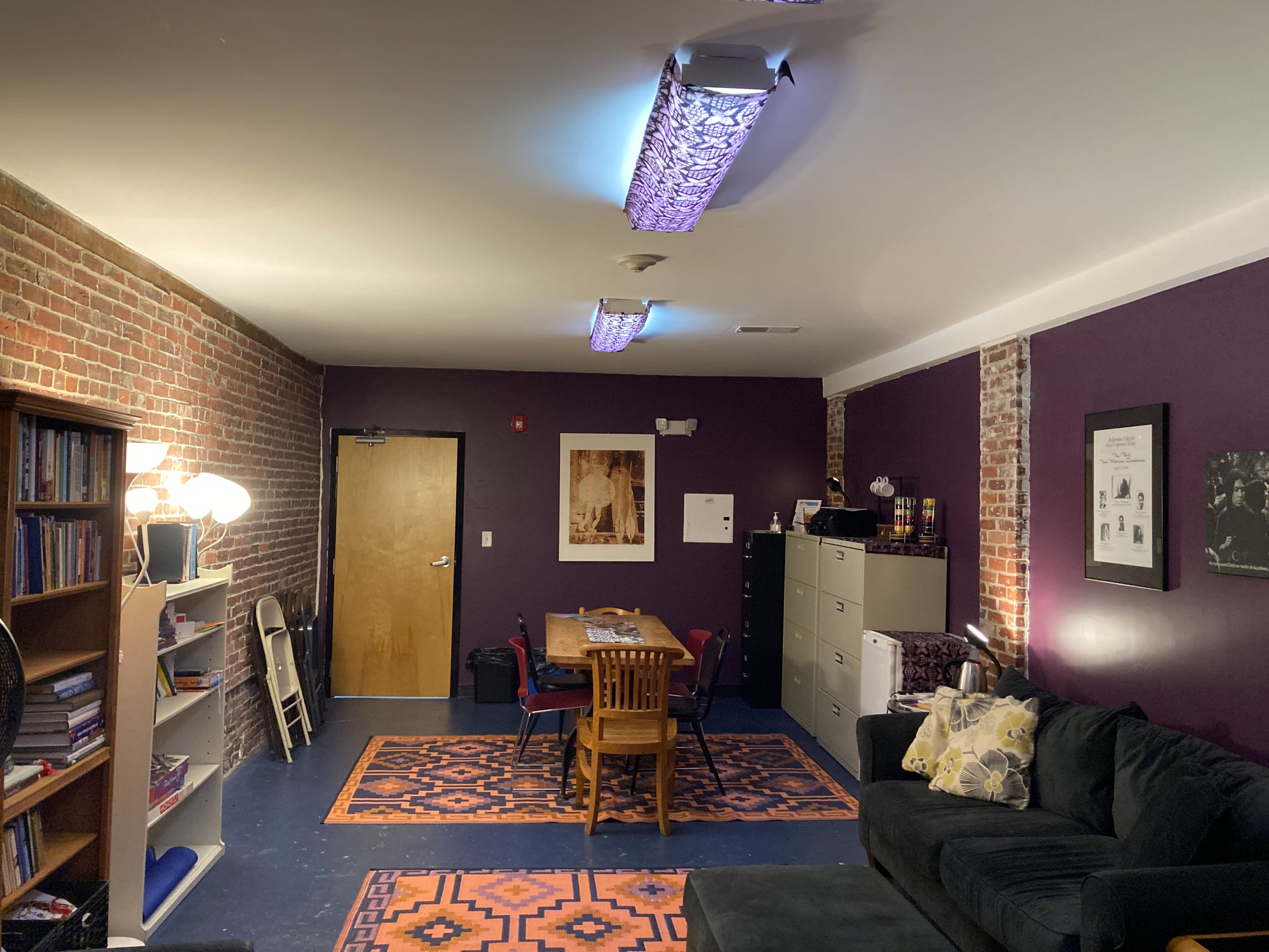 A group of eight people poses playfully during a rehearsal session in a room with exposed brick walls and a cozy atmosphere.