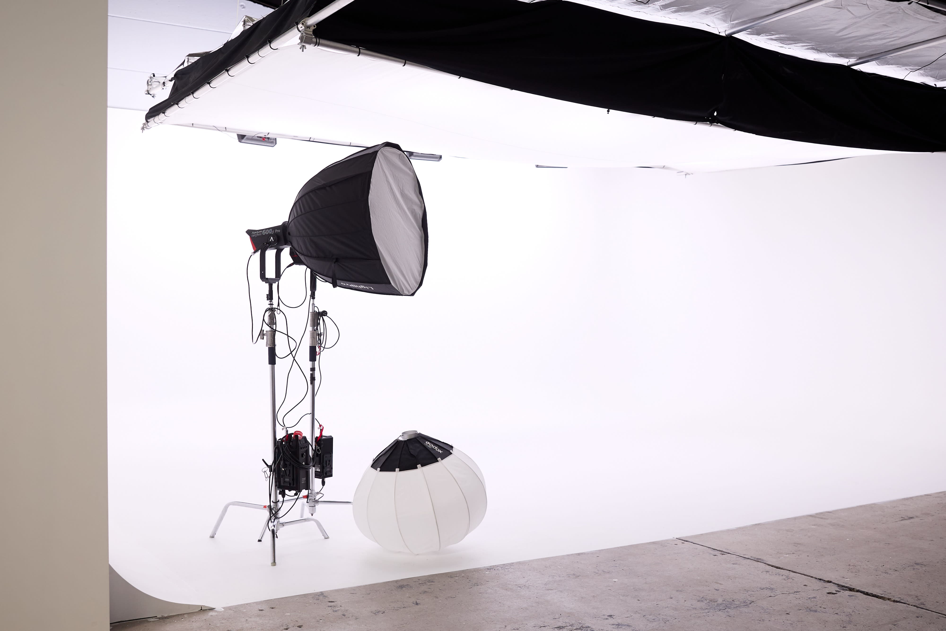 A photoshoot setup features a clothing rack with garments, a light stand, and a cart on wheels, all situated against a plain white backdrop.
