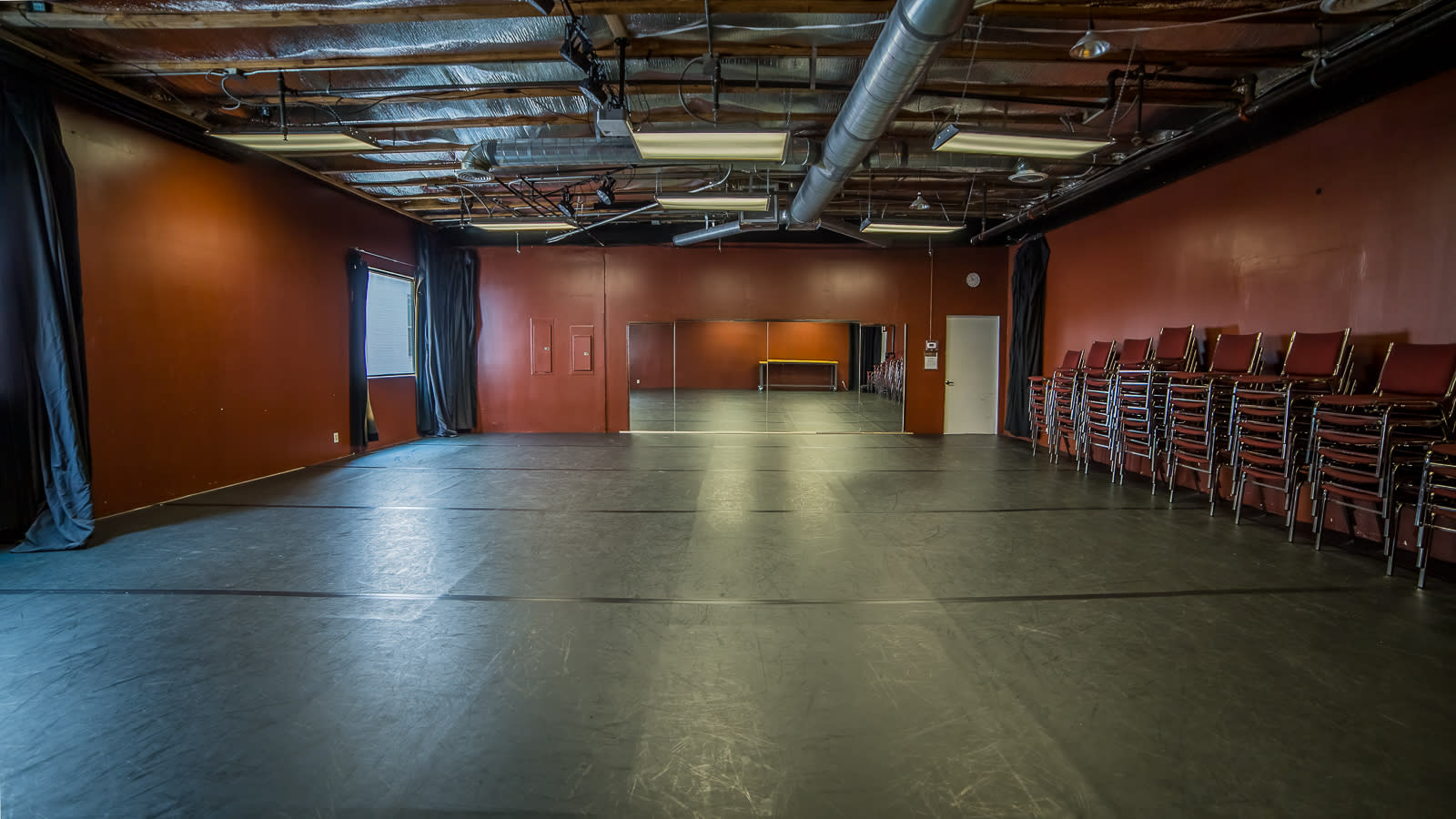 A dancer sits on a row of chairs in a dimly lit room, bending forward with her head down.