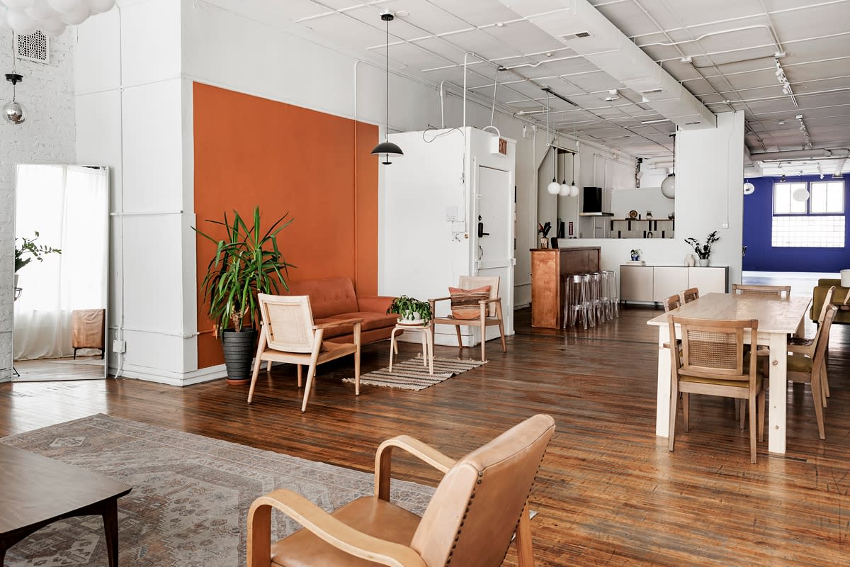 A corporate video shoot is taking place in a bright, minimalist room with large windows, showcasing plants and a mirrored wall.