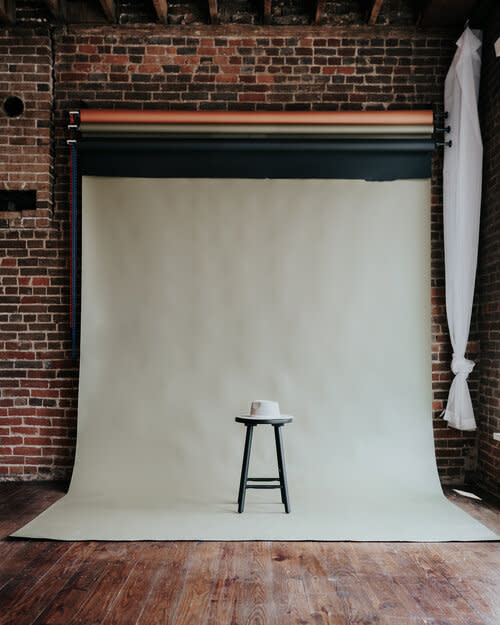 A woman stands beside a wooden ladder adorned with flowers, holding a bouquet of greenery in a studio setting.