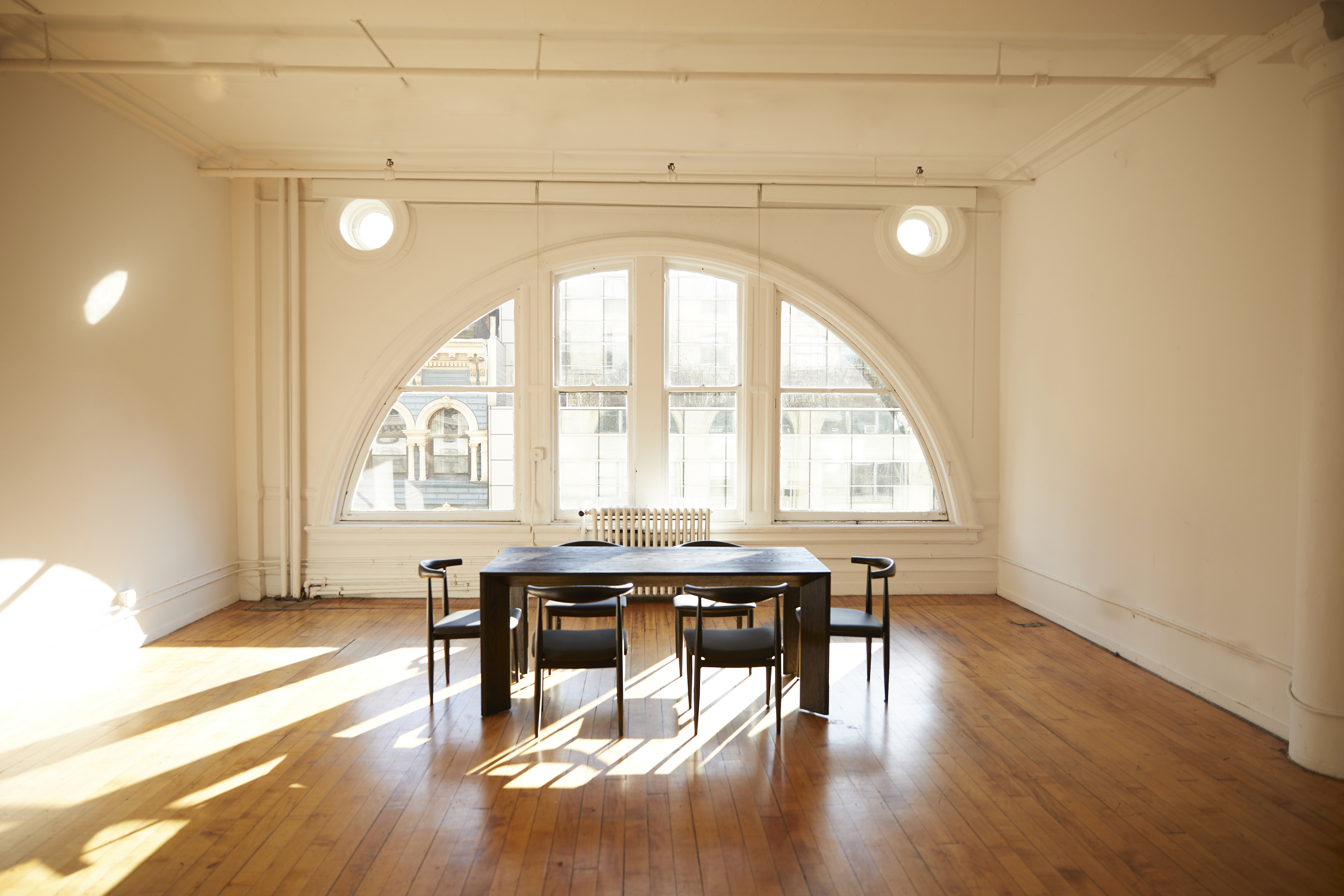 A dancer performs a high kick during a film shoot in a bright, spacious room with large windows.