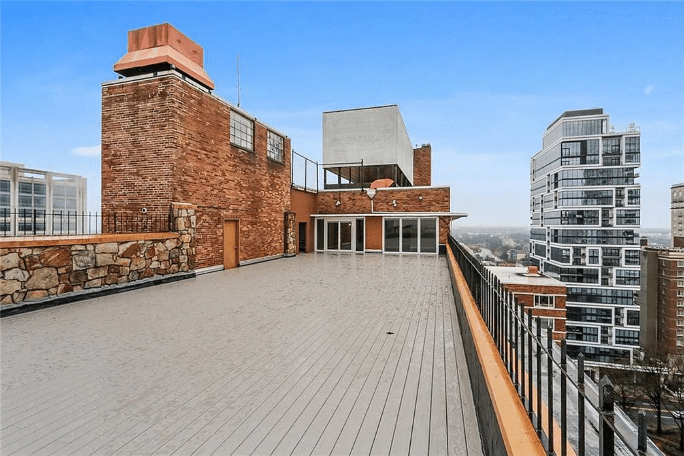A man in a black cardigan with a red heart design walks on a rooftop while being filmed by a camera.