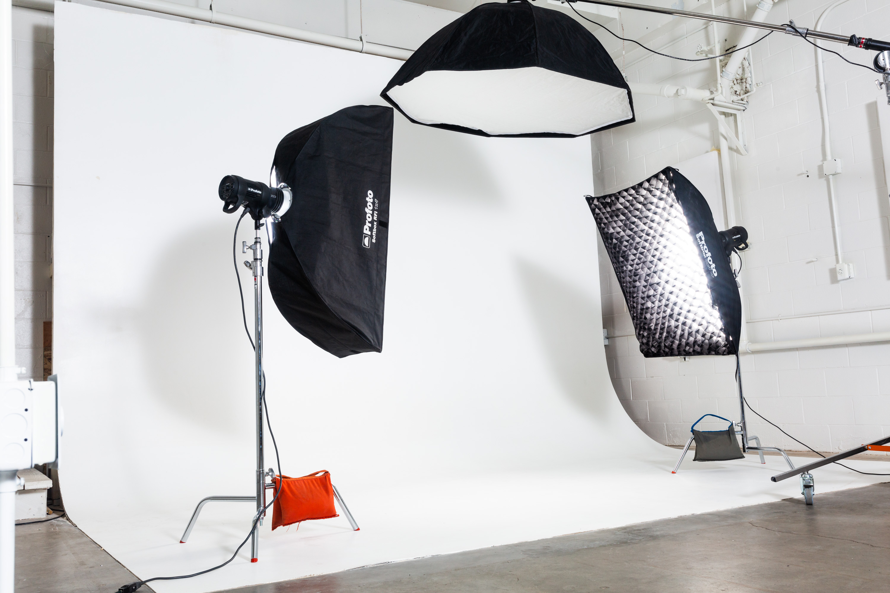 A photographer captures a model in front of a large white backdrop using multiple lights and equipment in a studio setting.
